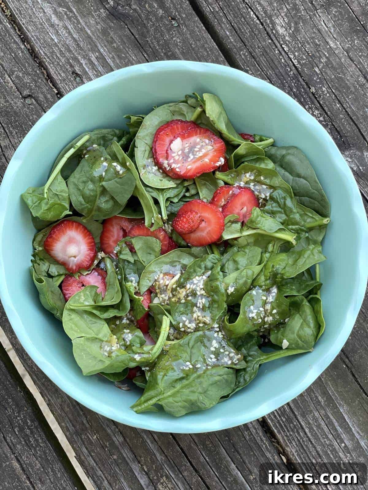 A beautiful blue bowl filled with strawberry and spinach salad, garnished with almonds and drizzled with the homemade sesame poppyseed dressing.