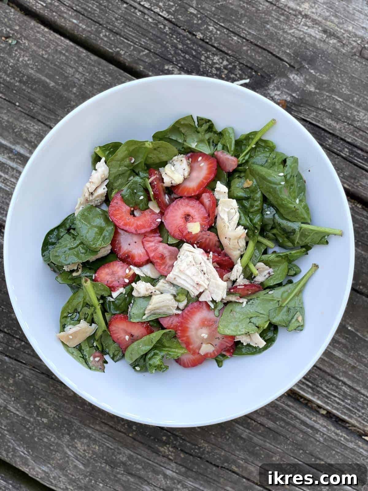 A pristine white bowl showcasing strawberry and spinach salad, complete with almonds and tender chicken, all tossed in the delightful sesame poppyseed dressing.
