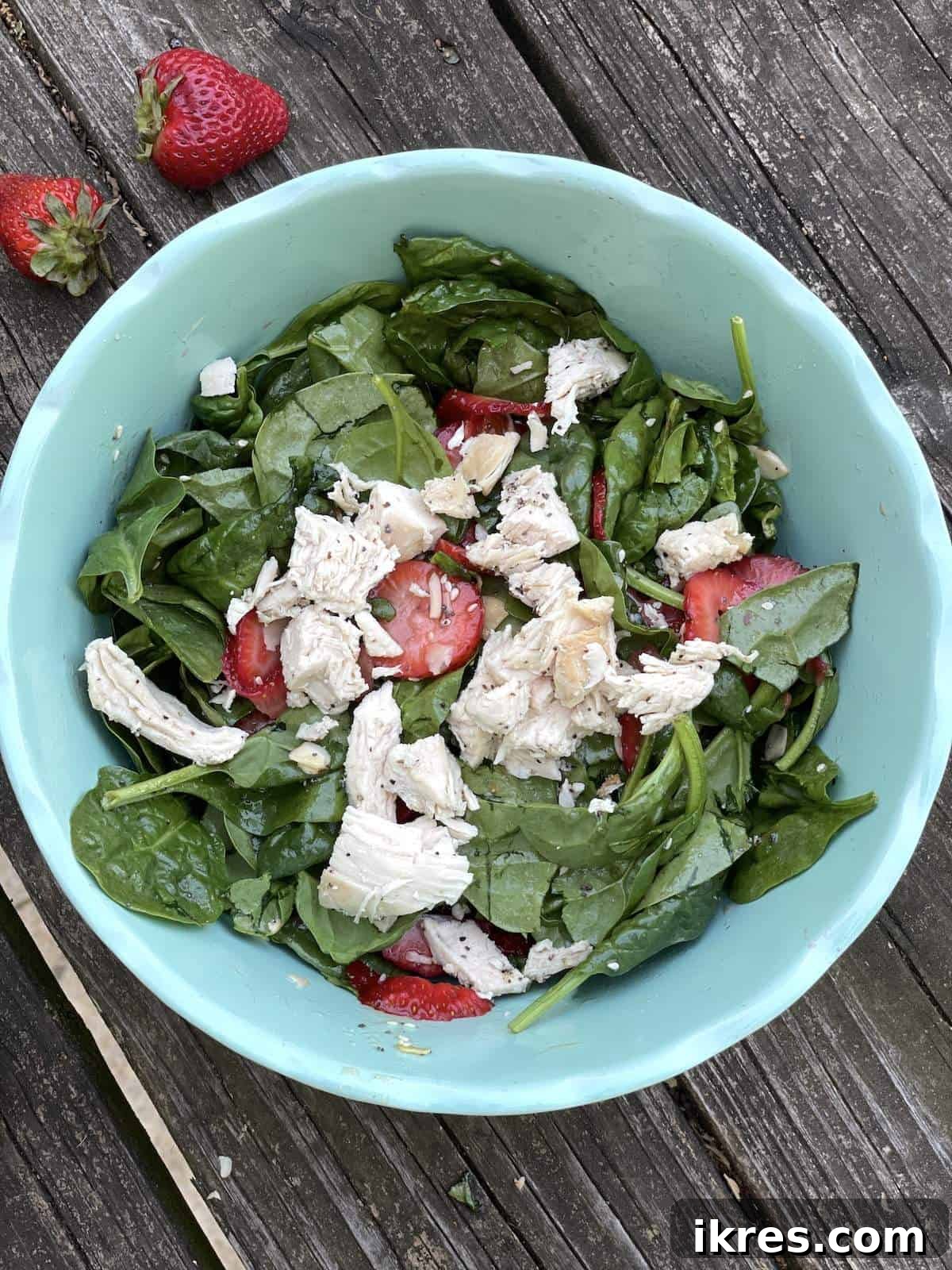A blue bowl showcasing a delightful strawberry and spinach salad with almonds, beautifully tossed in sesame poppyseed dressing, and crowned with succulent chicken pieces.