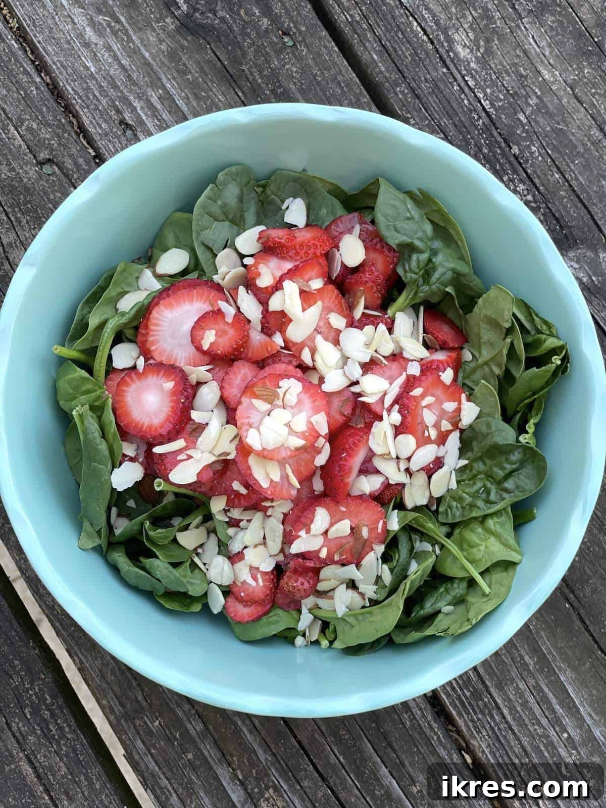 A bowl of fresh spinach and sliced strawberries, now generously topped with slivered almonds, awaiting the final toss.