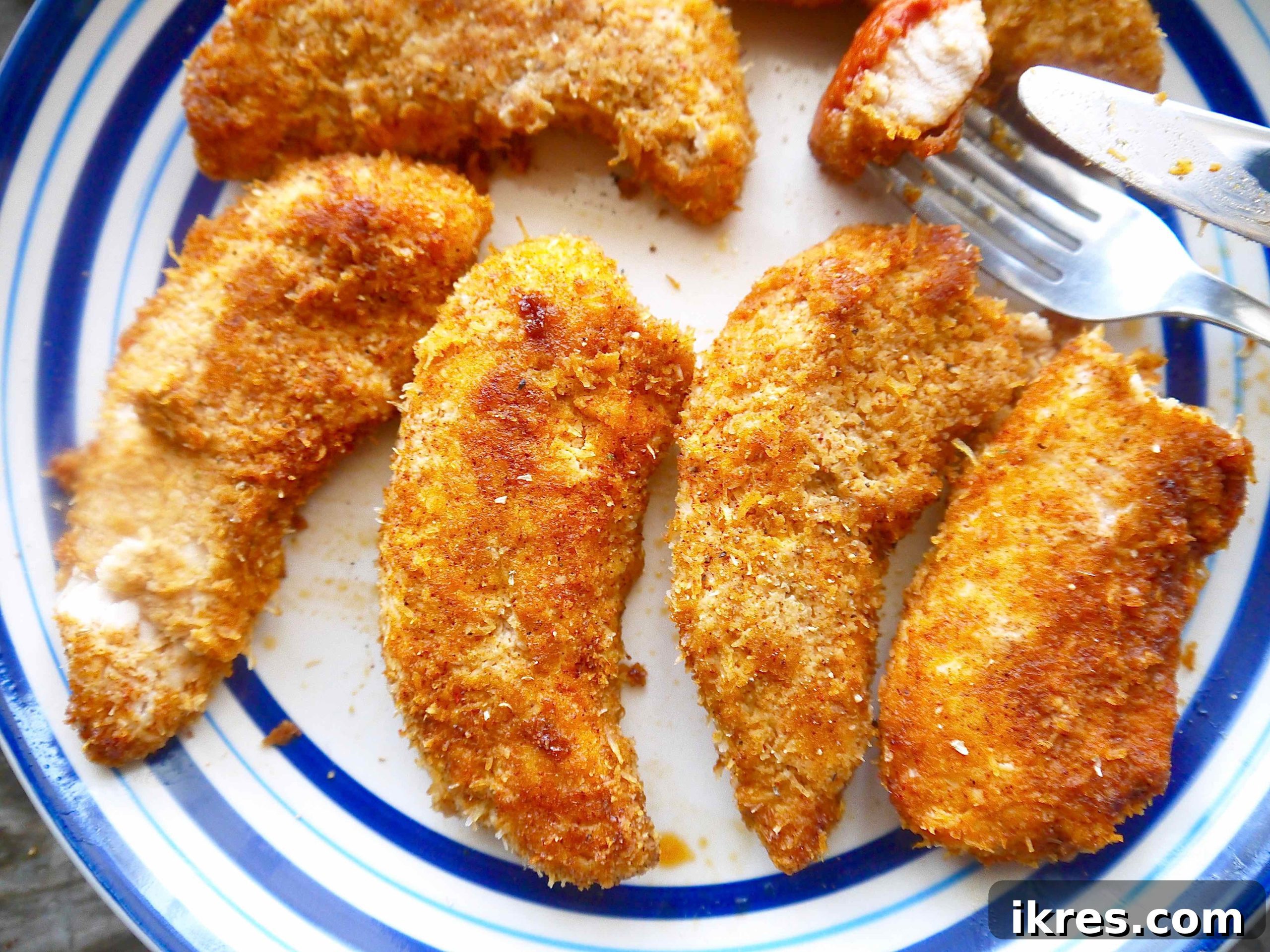 A close-up view of a baked almond flour chicken tender on a white plate, with a piece cut off to reveal the juicy interior.