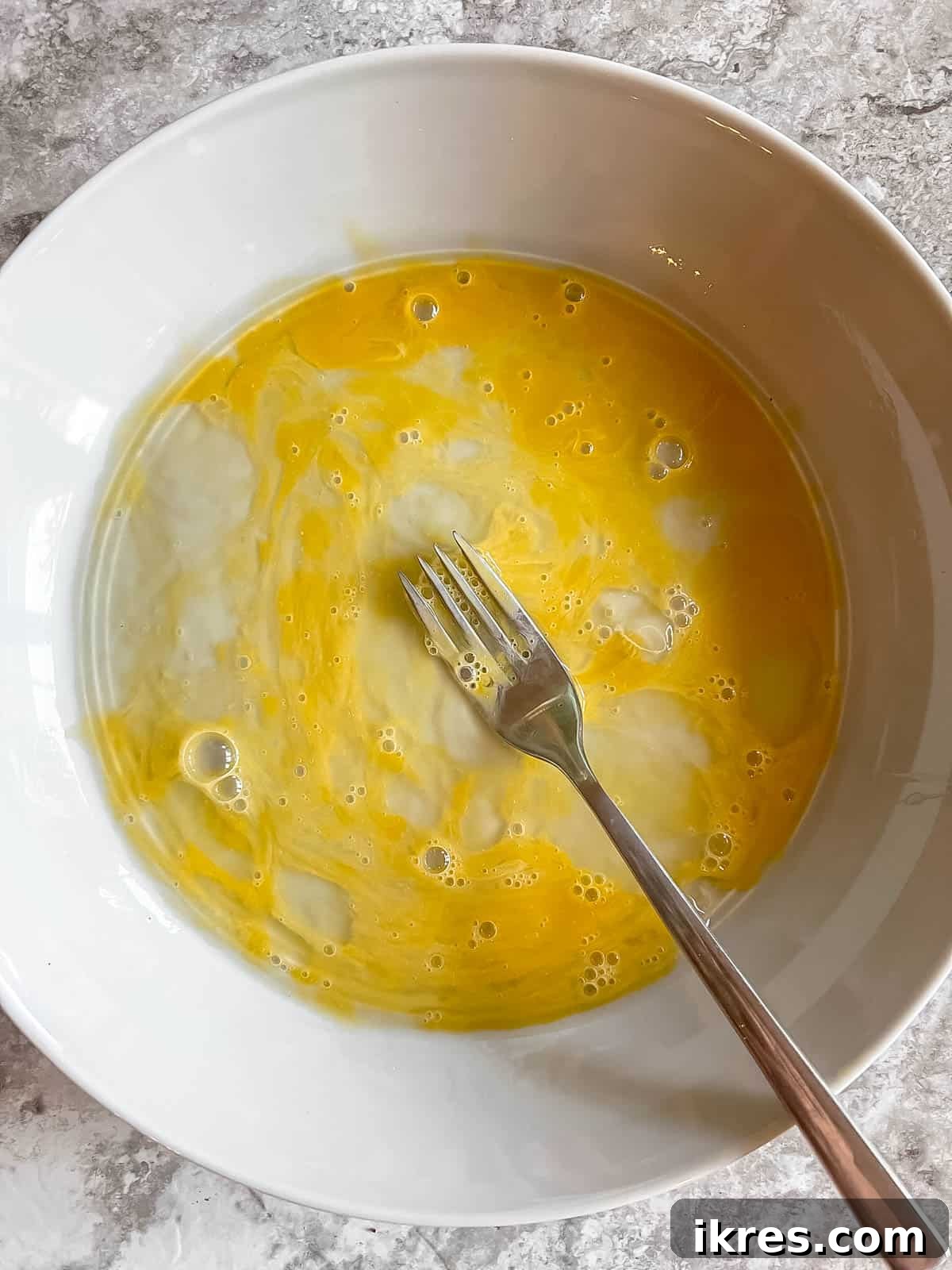 A single egg expertly whisked in a clear glass bowl, showcasing its smooth, yellow consistency.