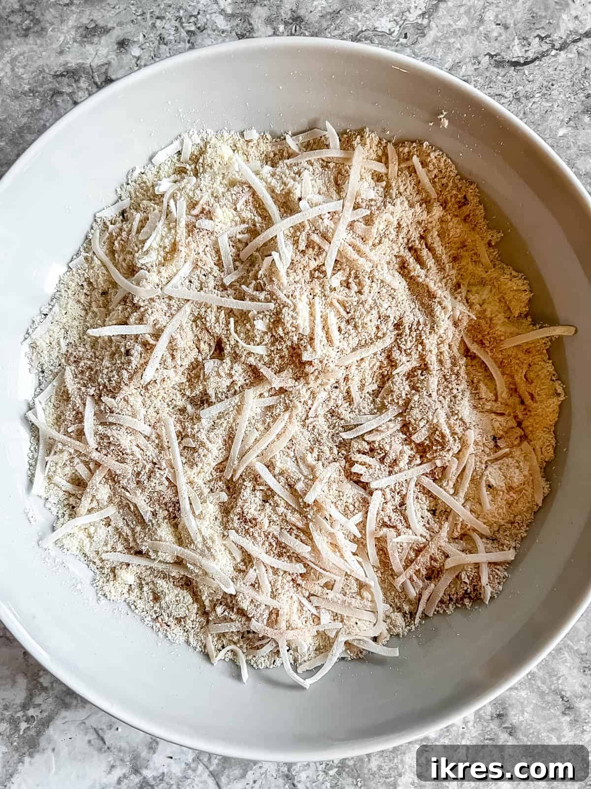 A bowl containing a dry mixture of almond flour, shredded coconut, and various spices, ready for breading.