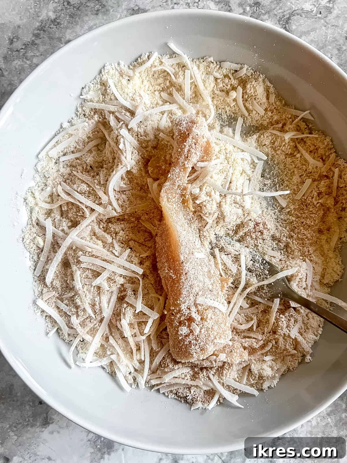 A chicken tender, first coated in egg wash, then thoroughly covered in the almond flour and shredded coconut breading mixture.