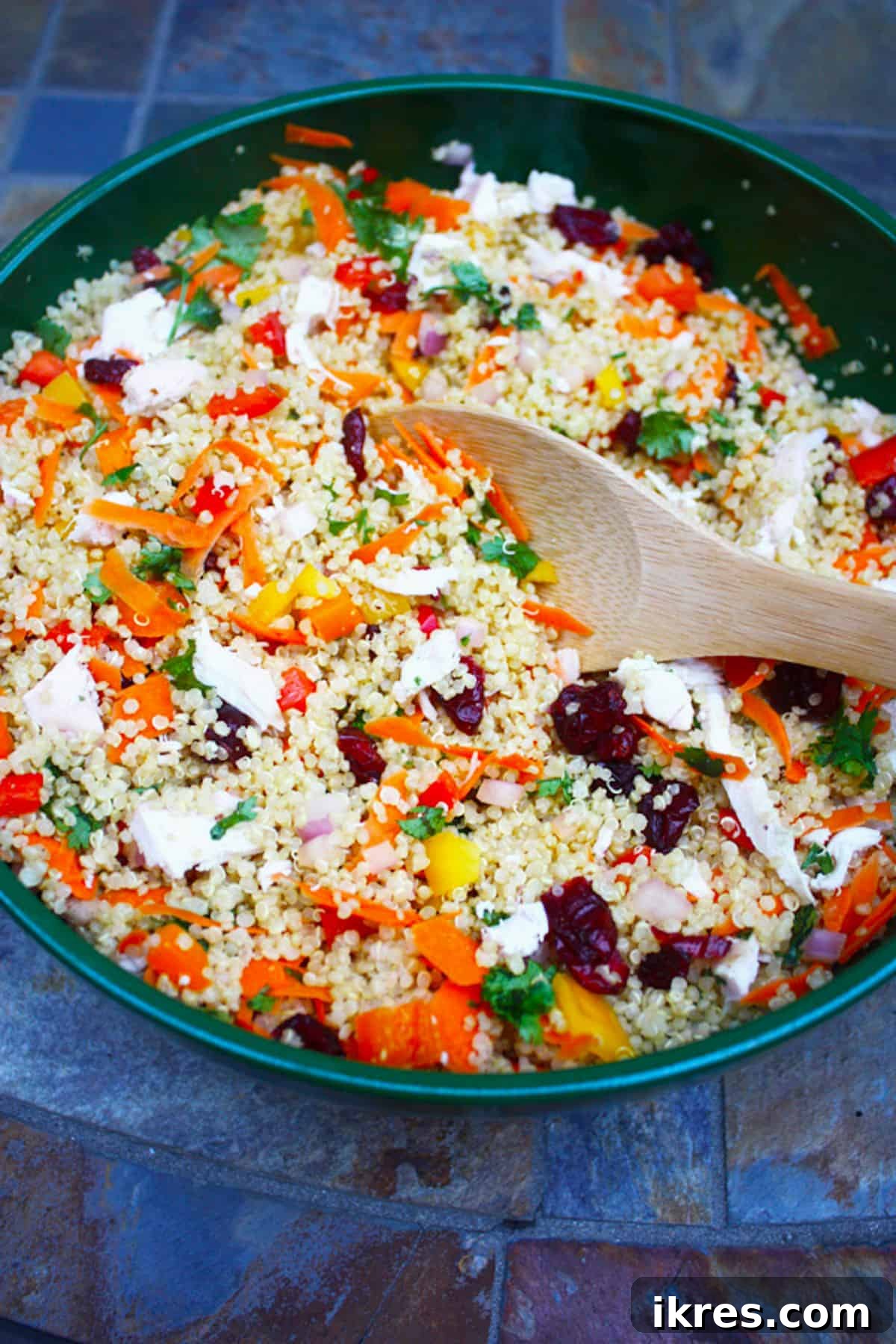A large green bowl brimming with colorful vegetable and chicken quinoa salad, ready to be served.