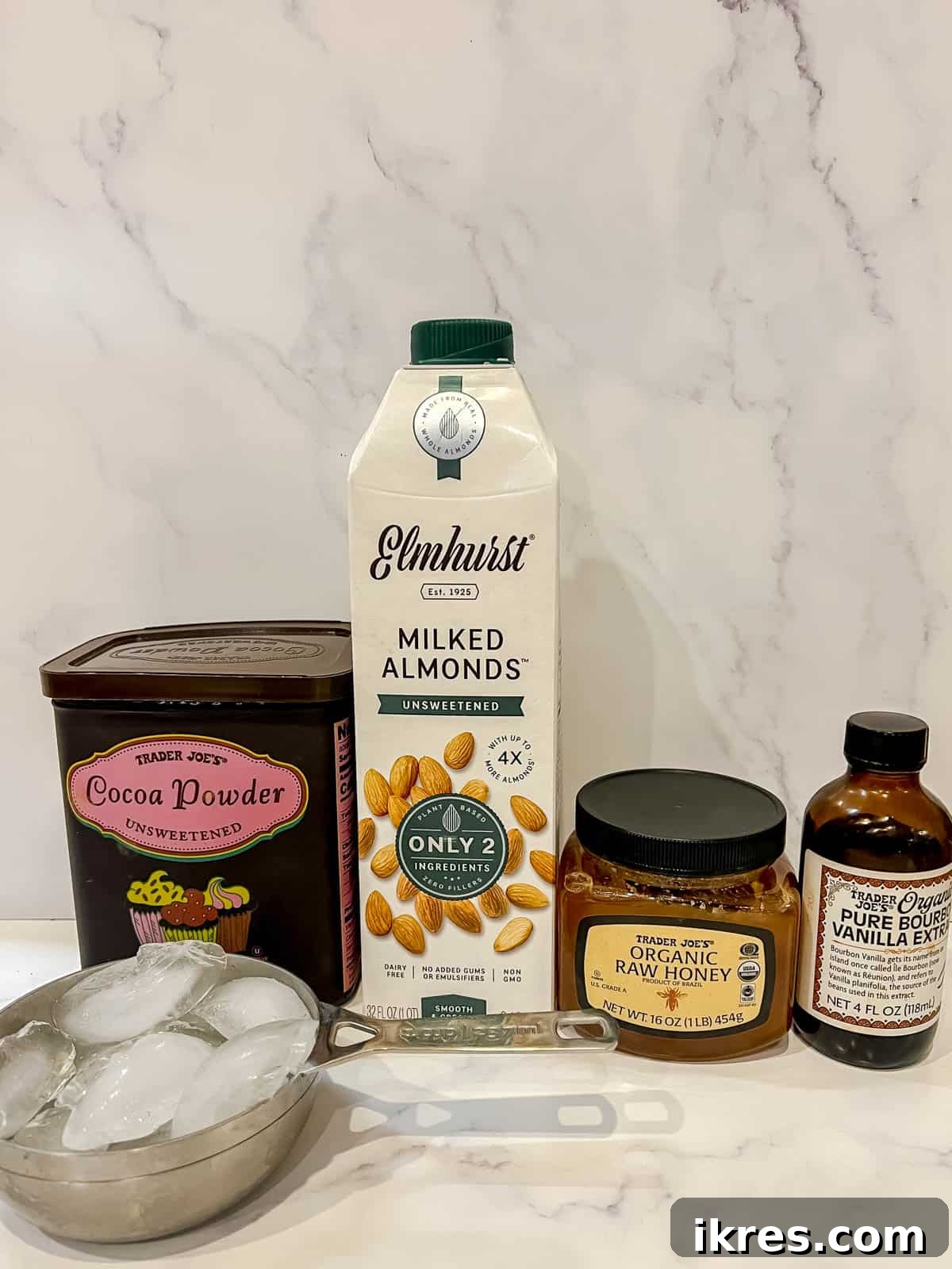 Paleo Frosted Chocolate Indulgence 3 Ingredients needed to make dairy-free frozen hot chocolate including honey, cocoa powder, plant-based milk, vanilla, and ice.