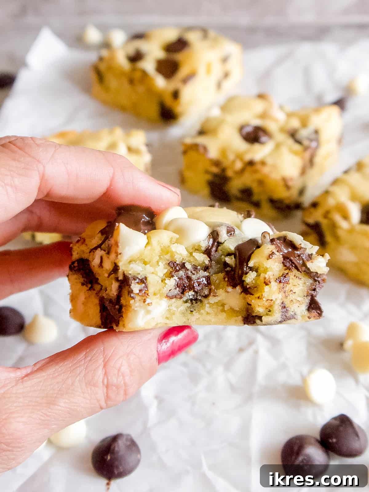 A hand holding a slice of white chocolate brownie with a bite taken out, showing the soft, melty center.