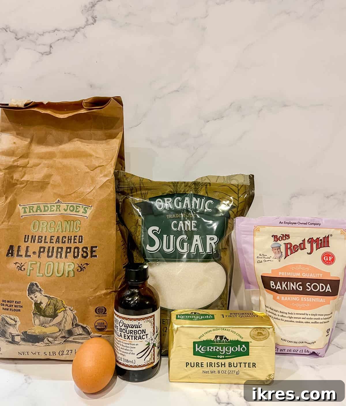A collection of essential ingredients for Sable Cut Out Sugar Cookies, including butter, flour, sugar, egg, and vanilla, neatly arranged on a counter.