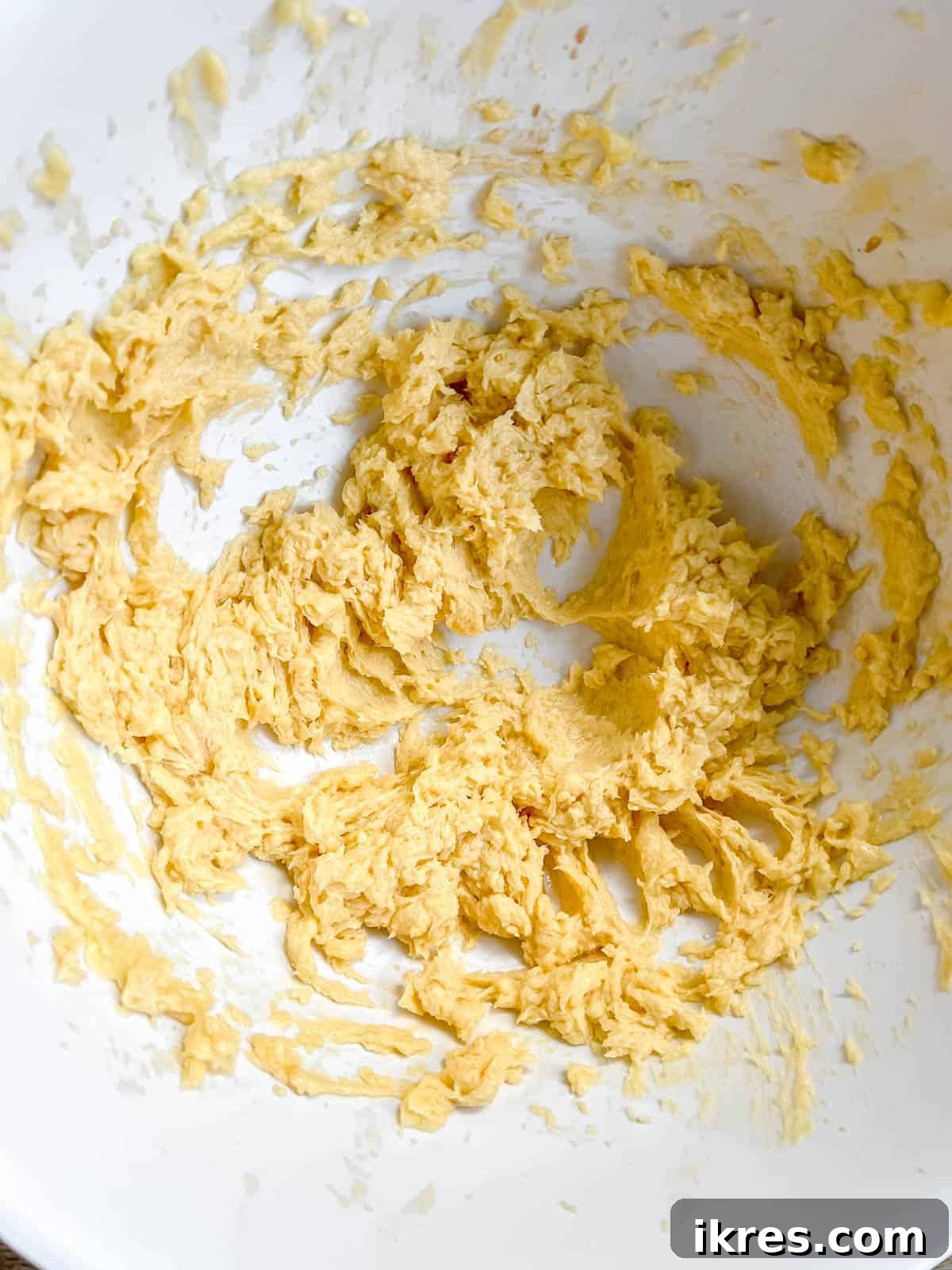 Softened butter and white sugar being creamed together in a mixing bowl with an electric hand mixer.