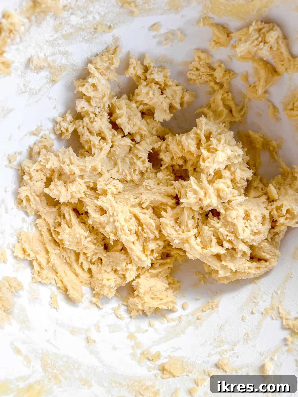 The first cup of flour being added to the cookie batter, beginning the transformation to a sandy texture.