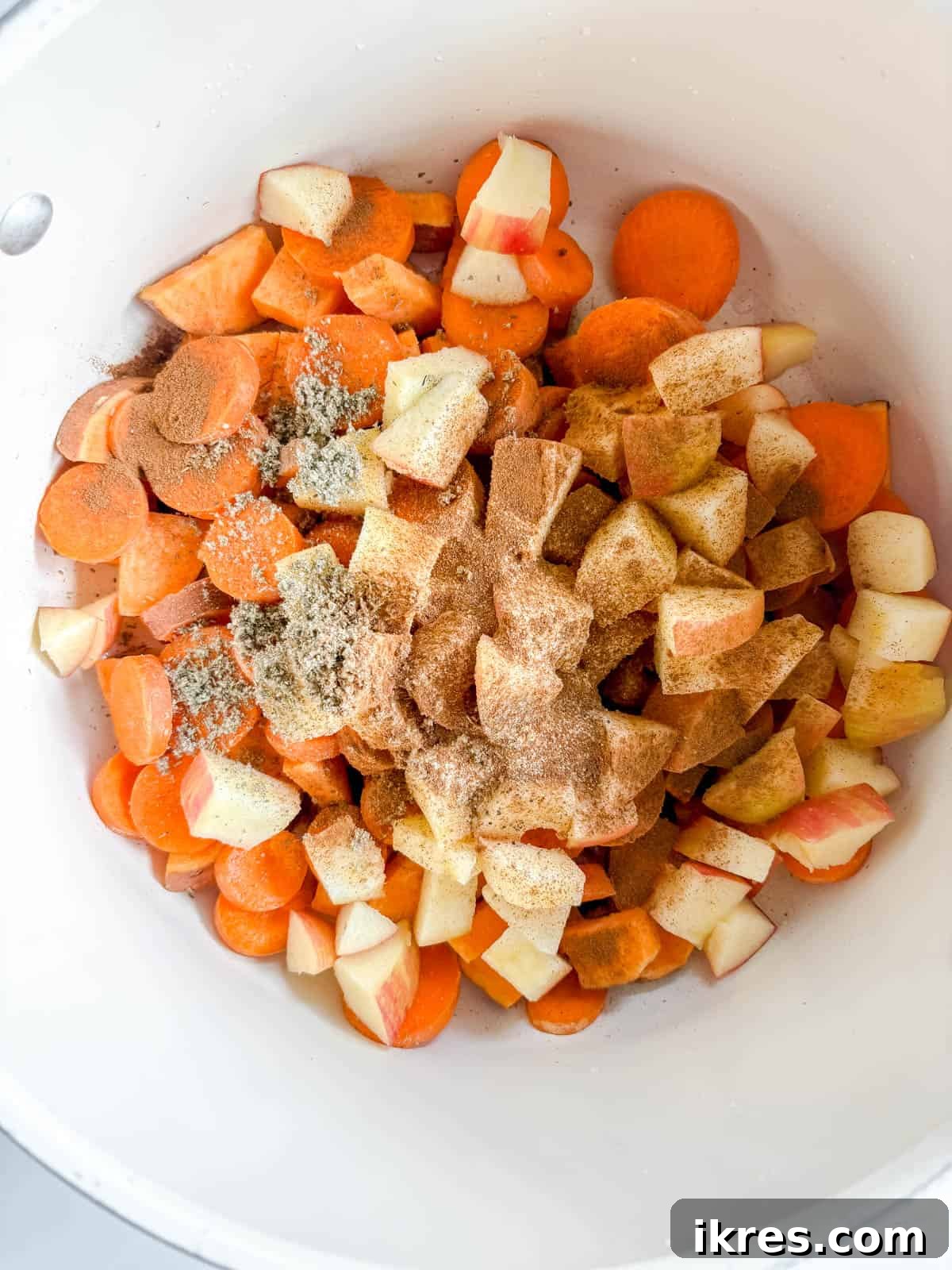 Sliced carrots, sweet potatoes, and diced apples seasoning in a pot.