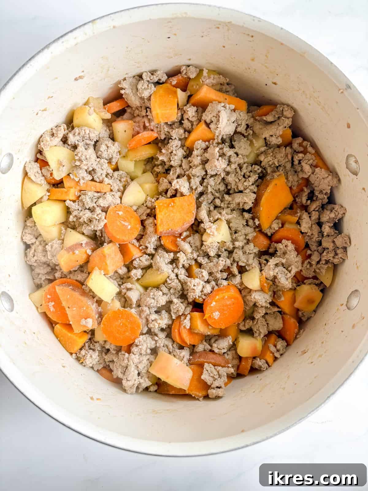 Ground turkey being added to the pot with the sautéed vegetables and apples.