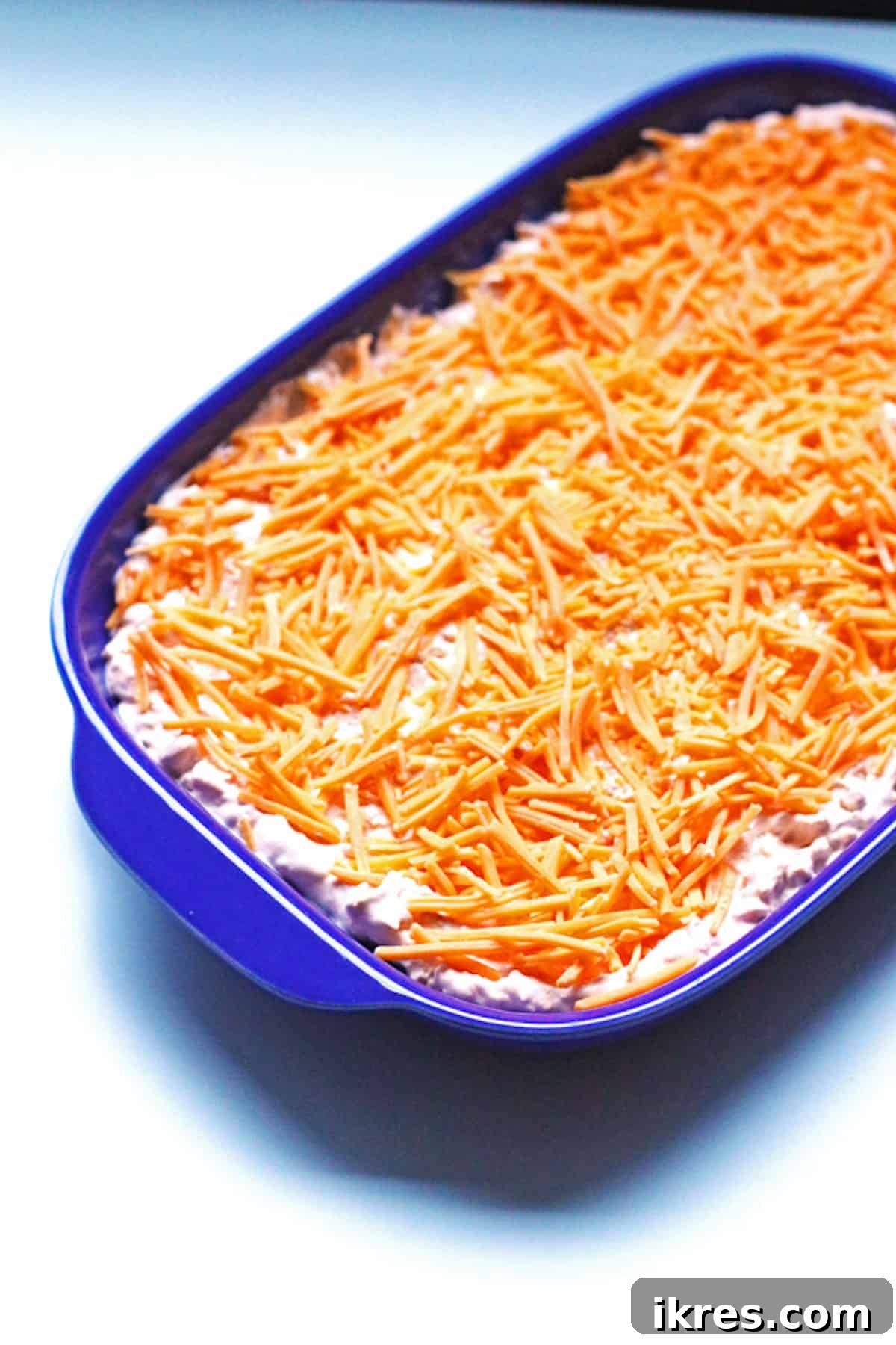 A tray of buffalo chicken dip topped with cheese that hasn't been baked yet.