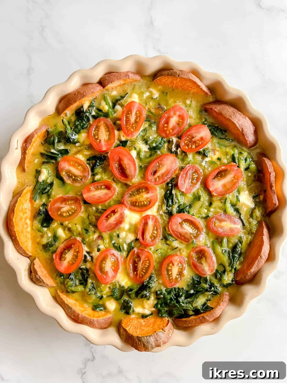 The assembled quiche before baking, with the zucchini and kale filling poured into the sweet potato crust and topped with halved cherry tomatoes.