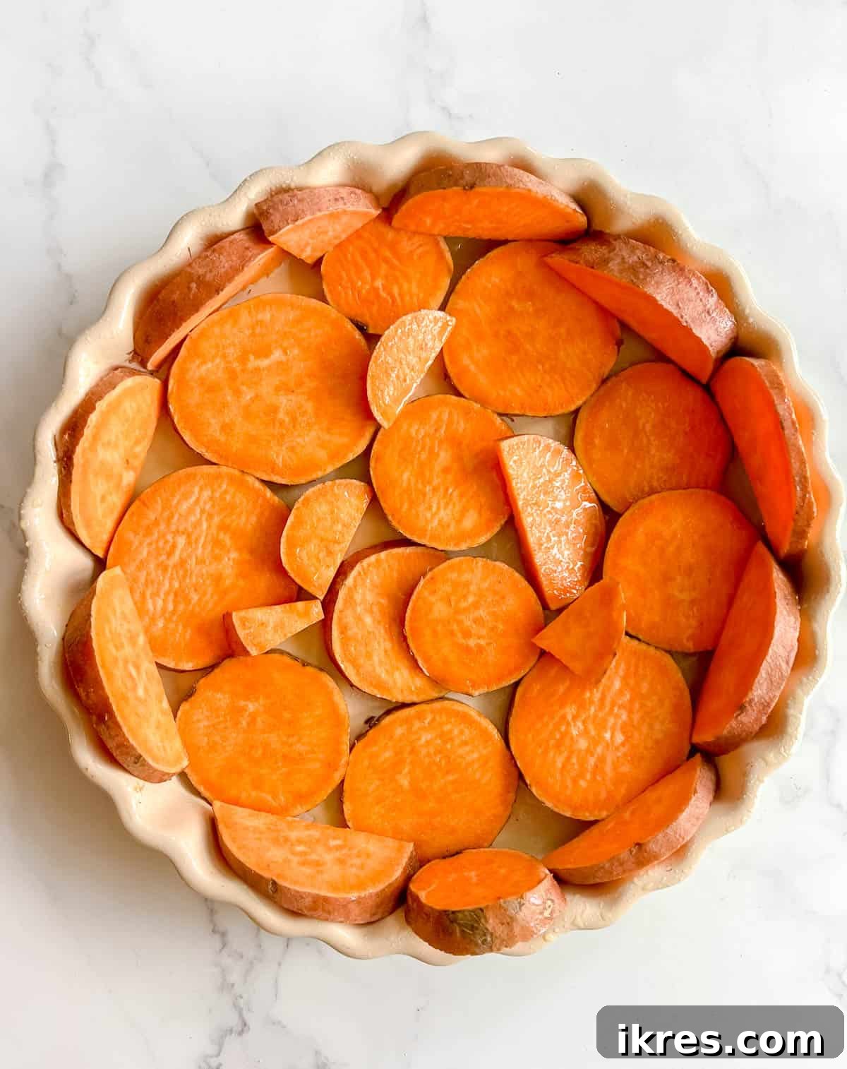 Thinly sliced sweet potatoes meticulously arranged in a round tart pan, forming the quiche crust before the initial baking stage.