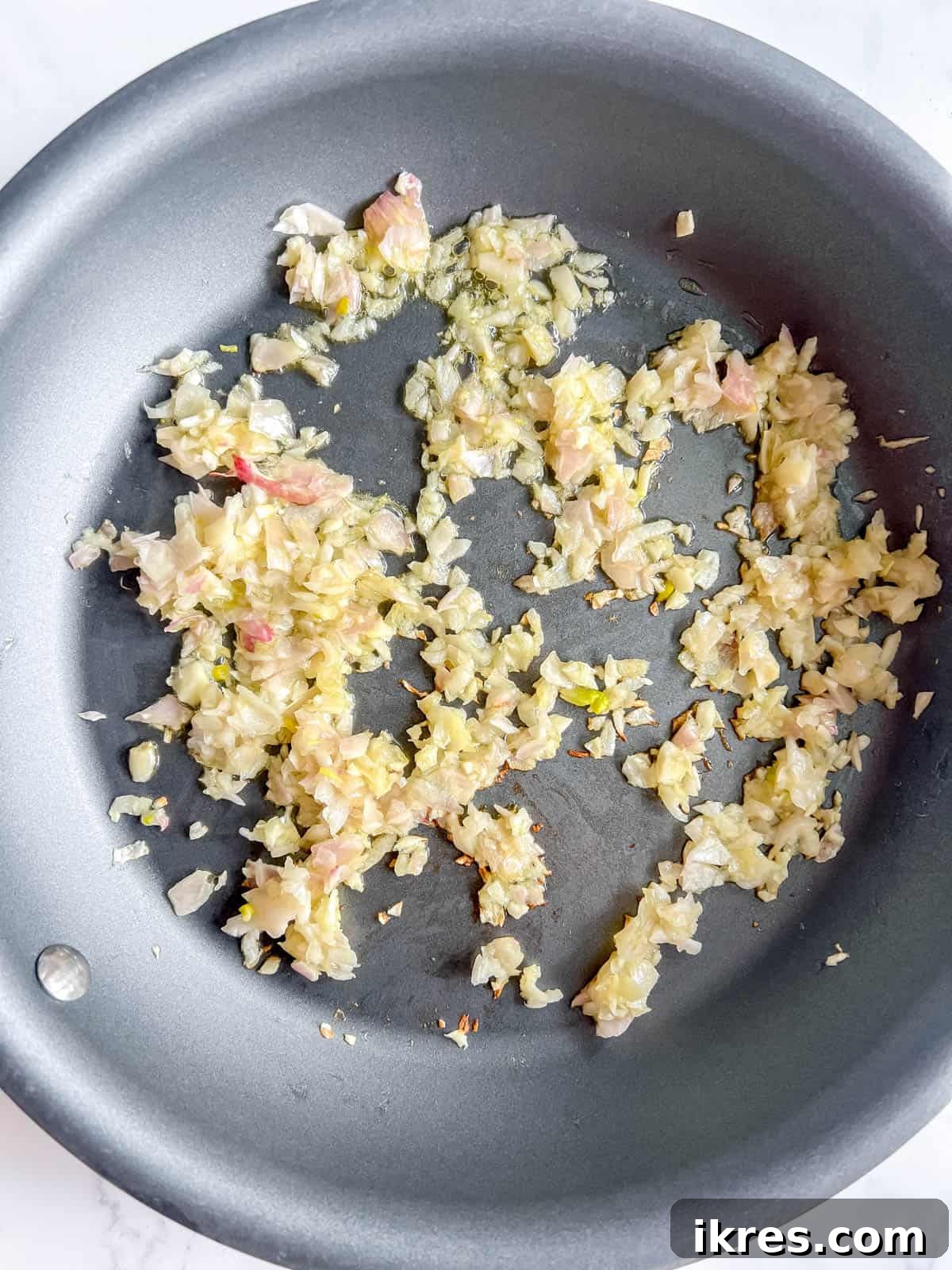 Minced shallot and garlic gently sautéing in a hot pan with olive oil, creating an aromatic base for the quiche filling.