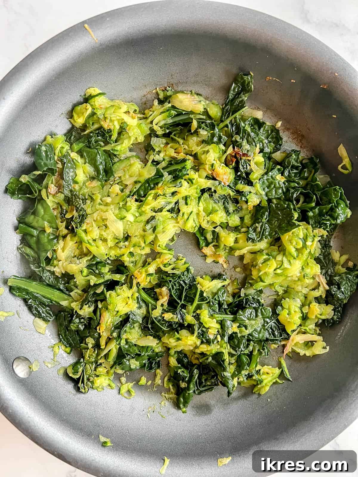 Cooked kale and shredded zucchini mixed with sautéed shallots and garlic in a pan, reduced and tender, ready for the quiche filling.