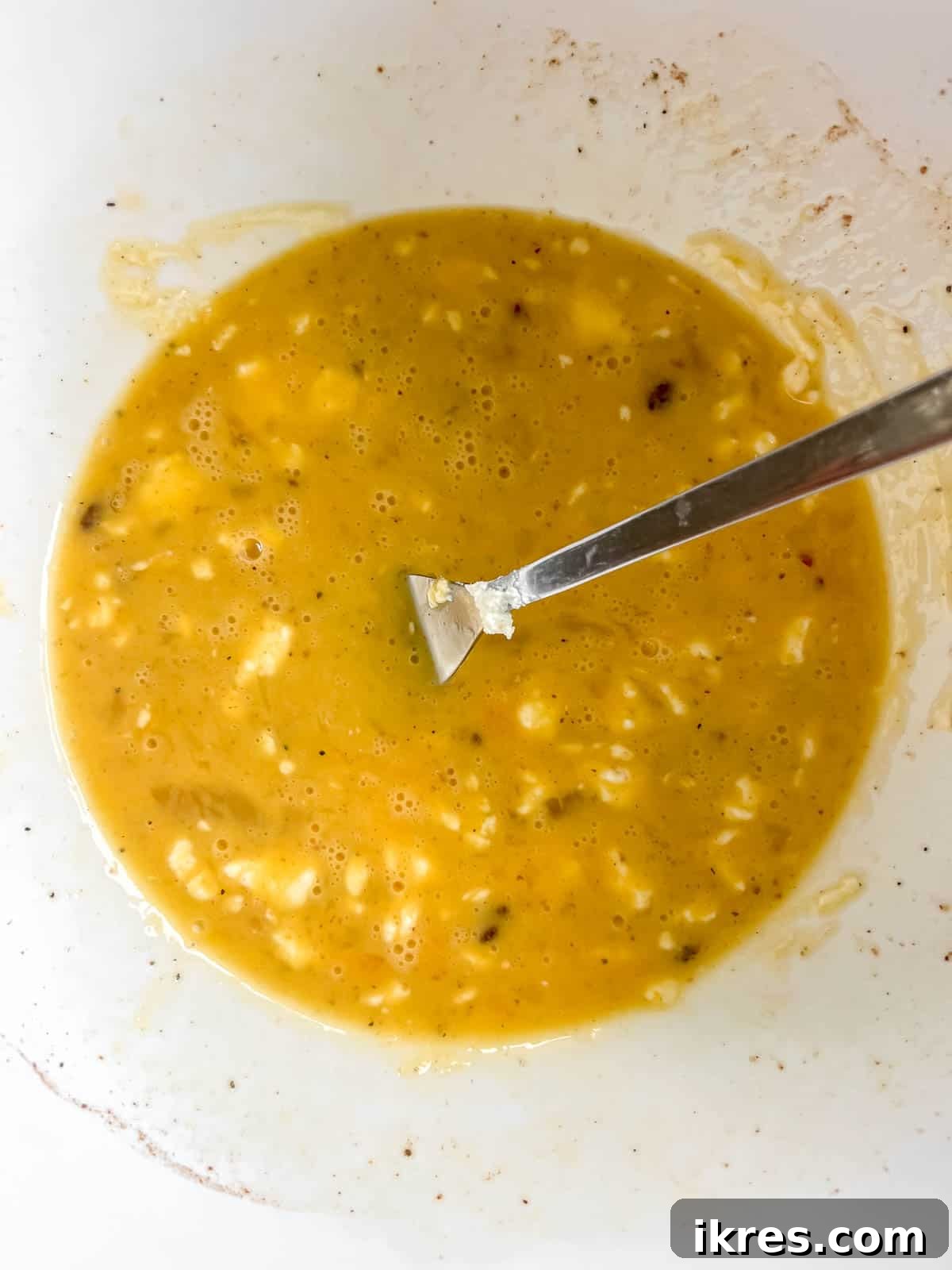 A bowl of whisked eggs, milk, salt, pepper, and nutmeg, forming the smooth, creamy base of the quiche custard mixture.