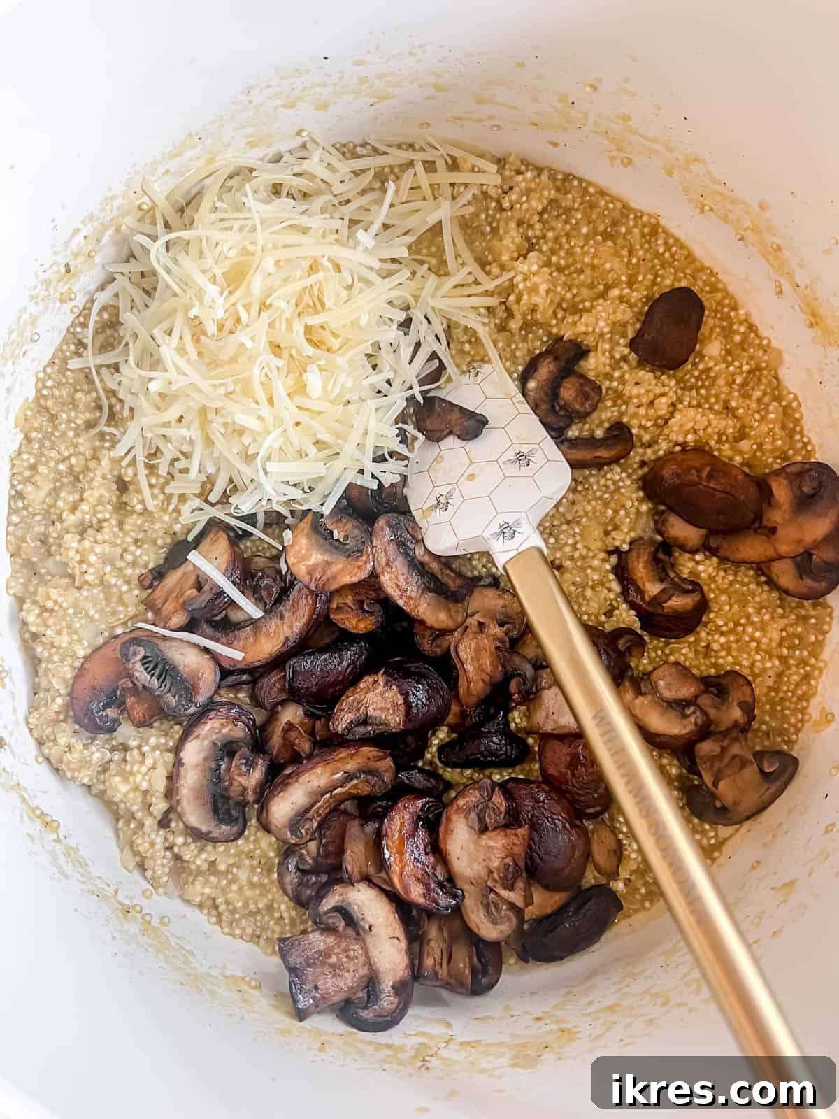 Cooked mushrooms and Parmesan cheese being folded into the creamy quinoa risotto in a large pan.