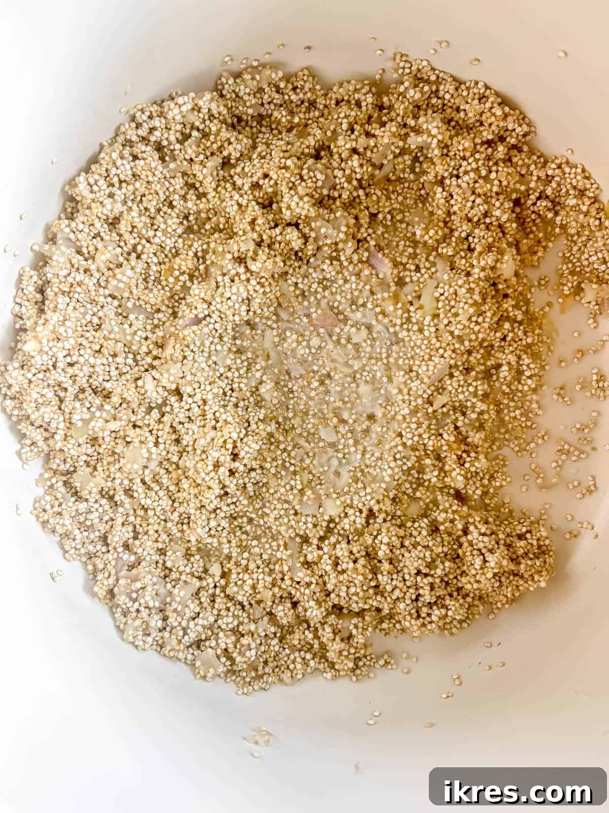 Rinsed quinoa being added to the pan with sautéed aromatics.