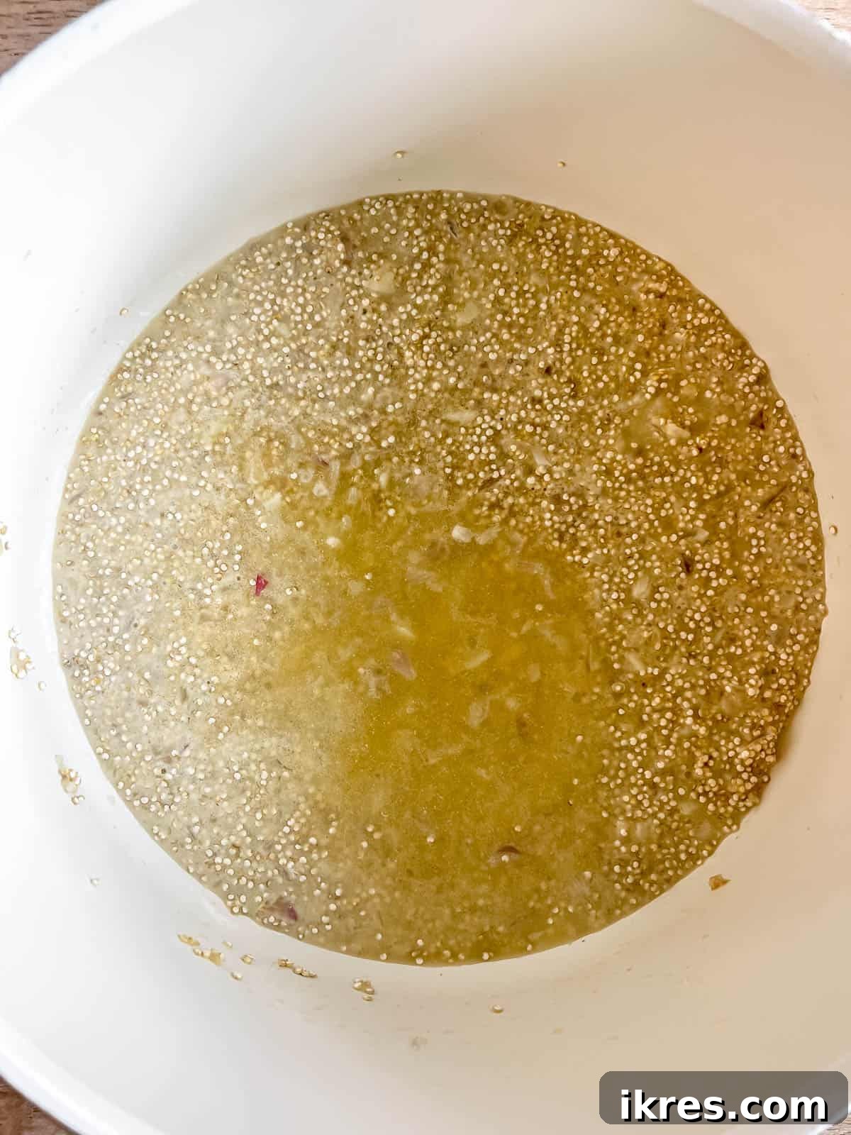 A ladle of chicken stock being added to the simmering quinoa in the pan.