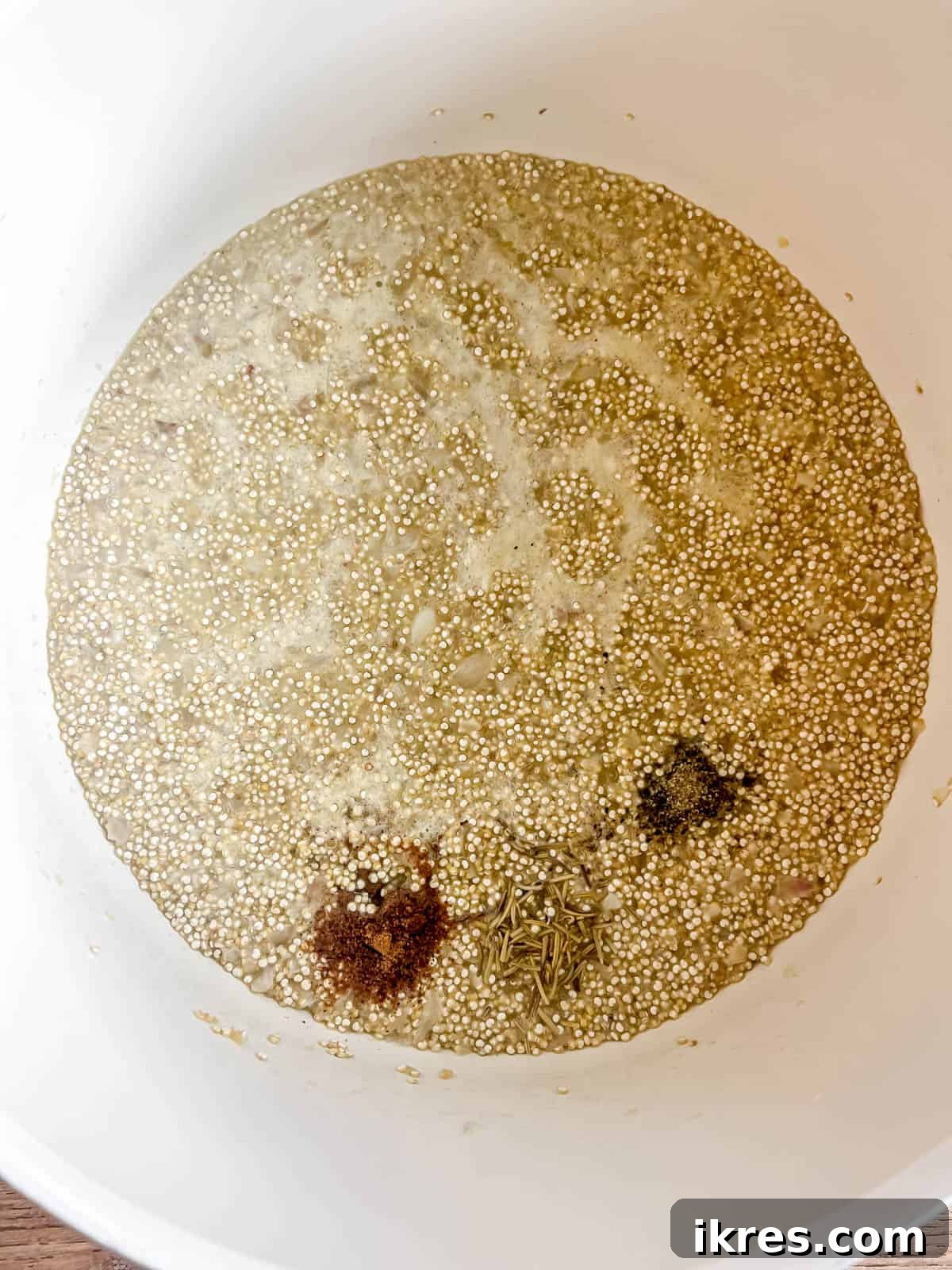 Ground nutmeg, dried rosemary, salt, and pepper being seasoned into the quinoa risotto.