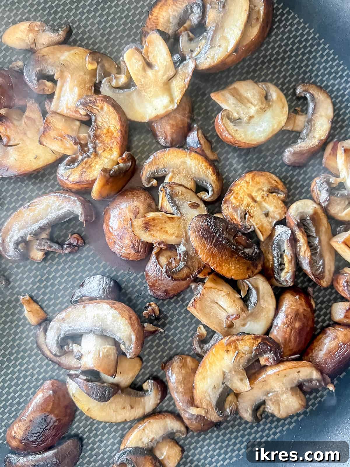 Sautéed baby bella mushrooms browning in a separate frying pan.