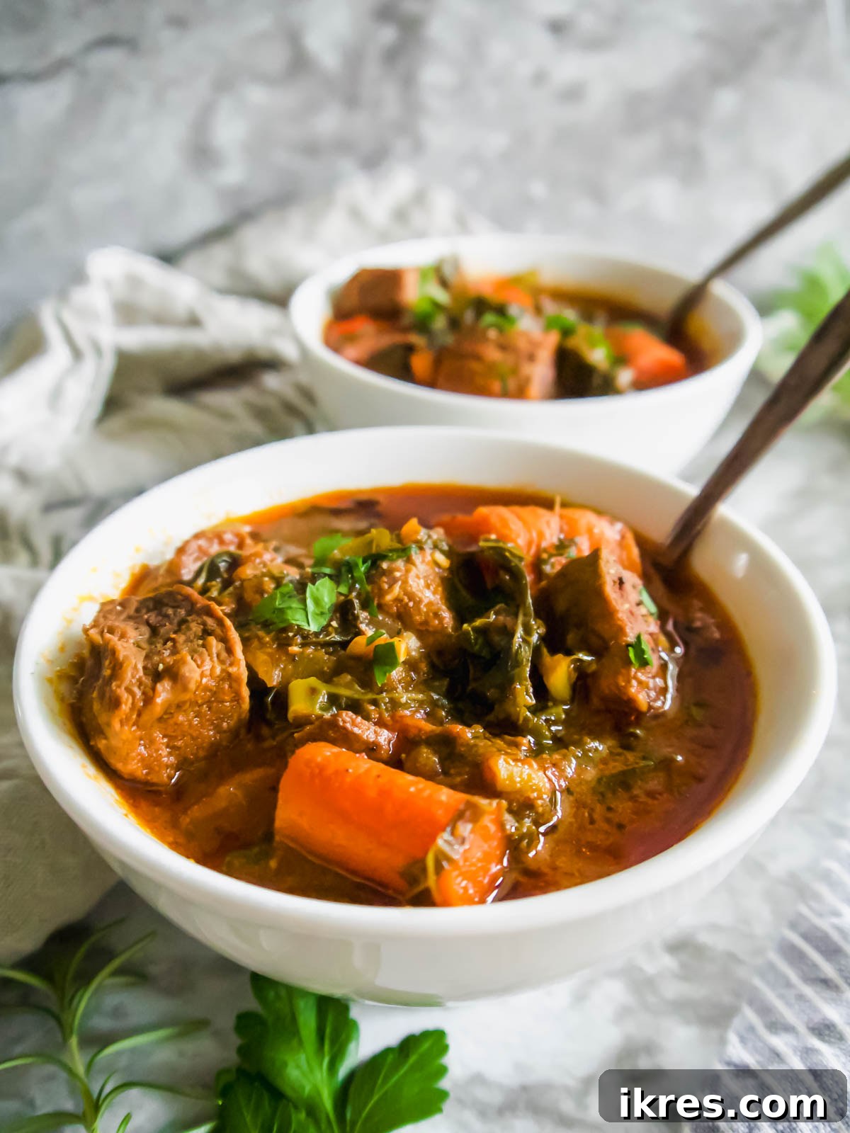 Nourishing Creamy Beef Stew with Kale and Tomato Paleo Gluten Free 3 Side angle of beef and kale stew in two bowls with spoons inside them.
