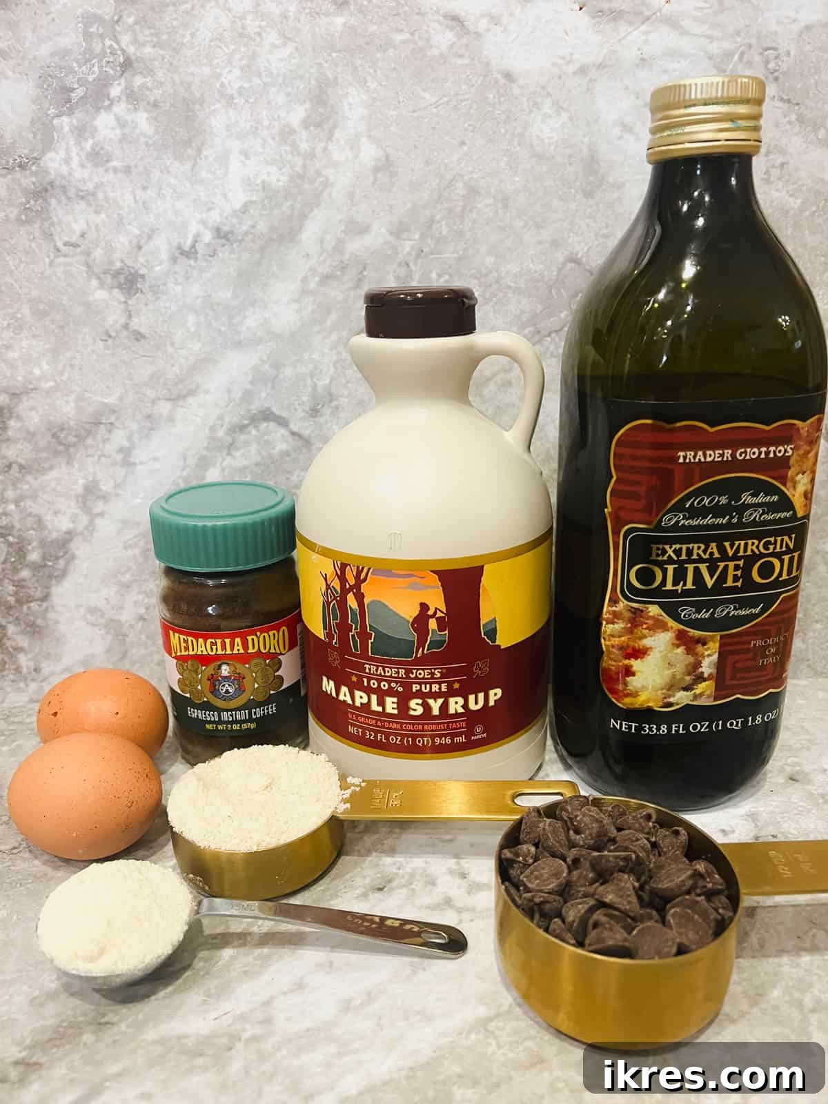 Decadent Gluten Dairy Free Molten Lava Cakes 3 Individual ingredients for gluten-free chocolate lava cake laid out on a white surface, including olive oil, maple syrup, chocolate chips, eggs, almond flour, coconut flour, and instant espresso.