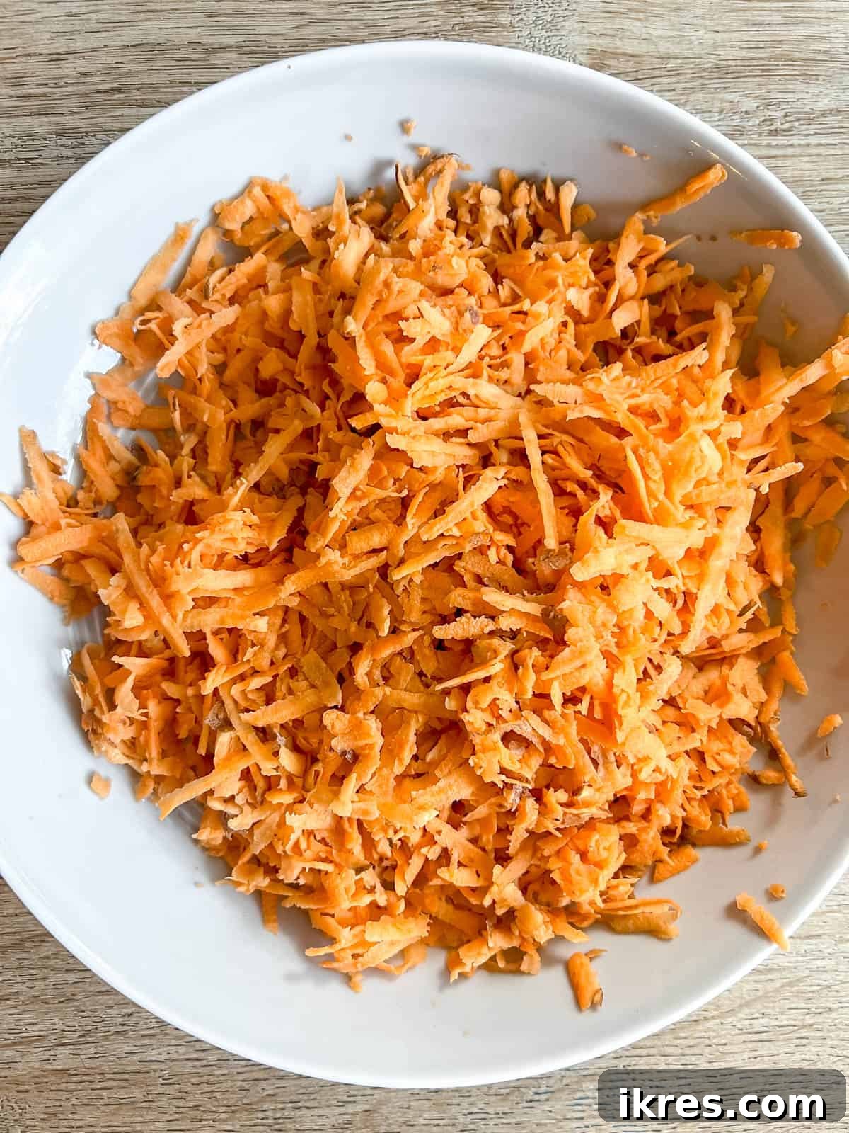 A bowl filled with finely shredded sweet potato, glistening and ready to be mixed into the egg base.