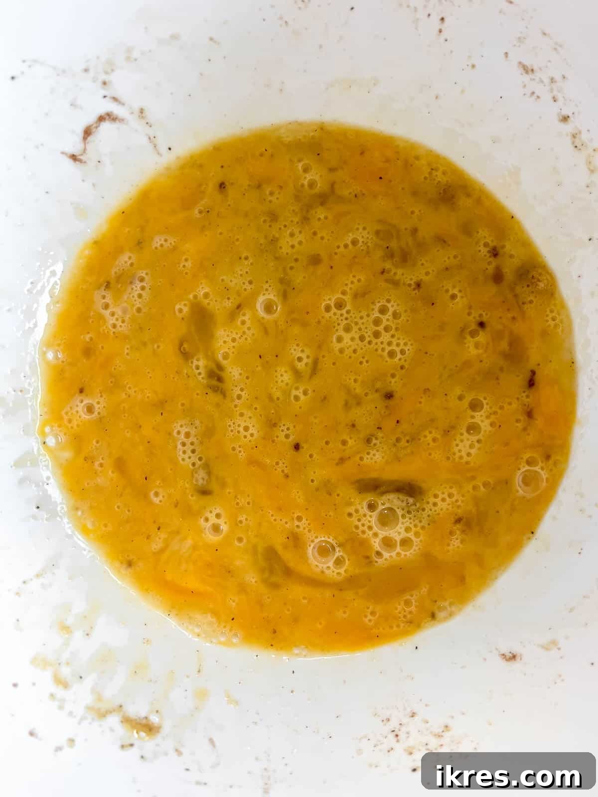 A mixing bowl containing whisked eggs perfectly blended with various seasonings, creating a smooth, pale yellow mixture.