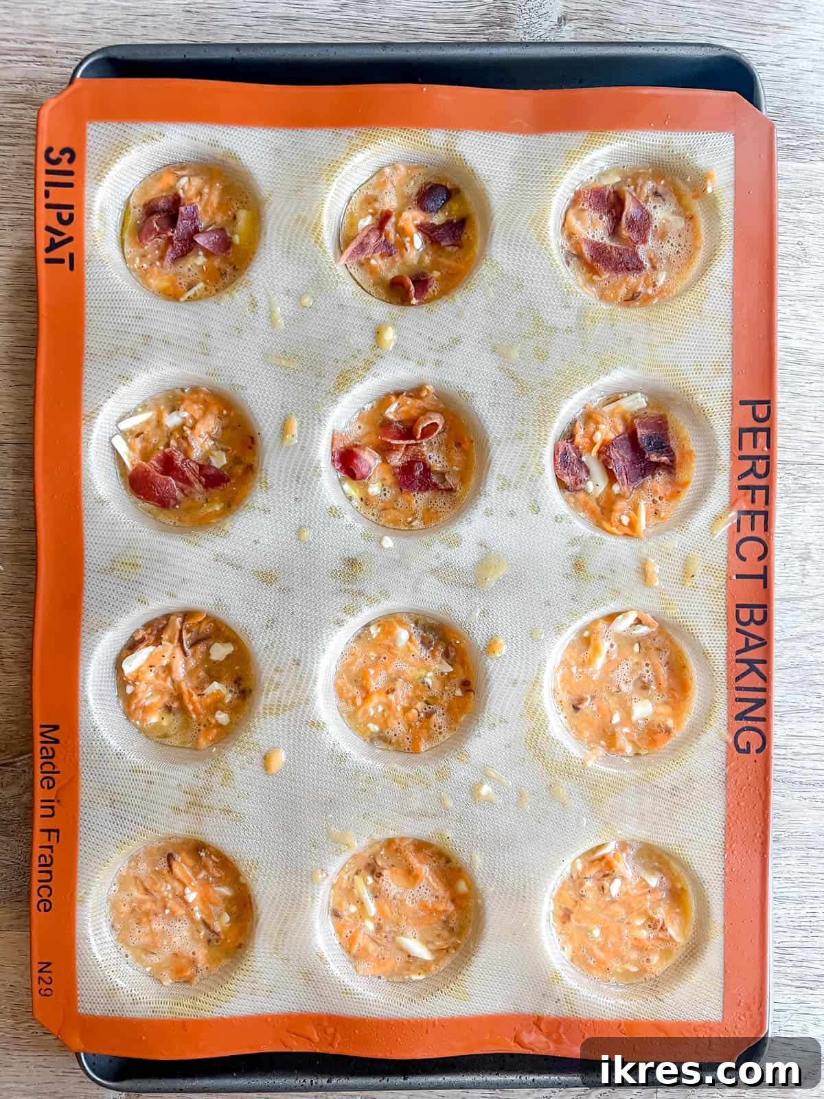 Silicone muffin cups filled with the sweet potato and egg mixture, neatly topped with crumbled bacon before baking.