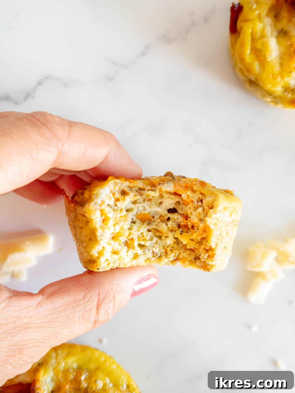 A single sweet potato and bacon breakfast muffin with a bite taken out, revealing the fluffy interior and vibrant shredded sweet potato texture.