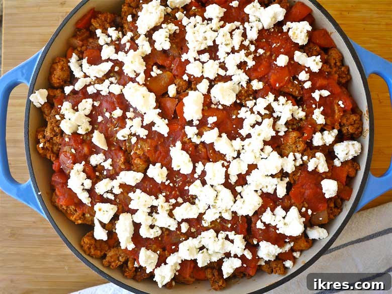 Layered enchilada casserole before baking, showing sweet potato, ground turkey, and cheese layers.