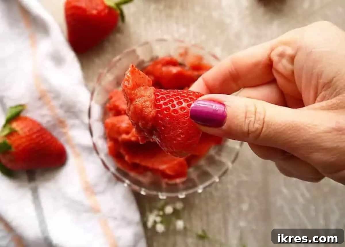 A fresh strawberry being dipped into a creamy pink strawberry mango sorbet, highlighting its vibrant color and luscious texture.