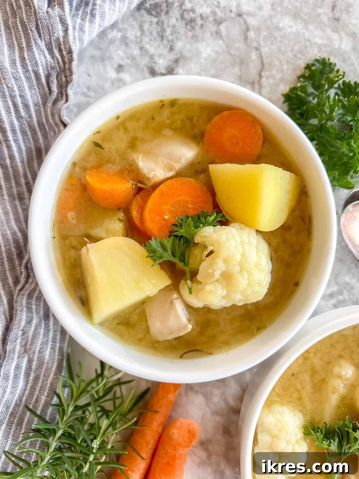 Nourishing Grain-Free Chicken Soup 2 A steaming bowl of vibrant Paleo Chicken Soup, rich with chicken, carrots, and other vegetables, on a rustic wooden table.