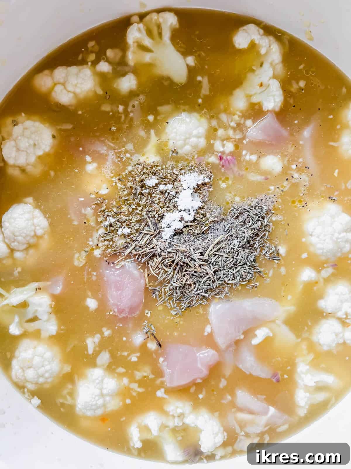 Nourishing Grain-Free Chicken Soup 6 The soup pot now contains chicken pieces, chicken broth, and a colorful array of herbs and spices, ready to be simmered.