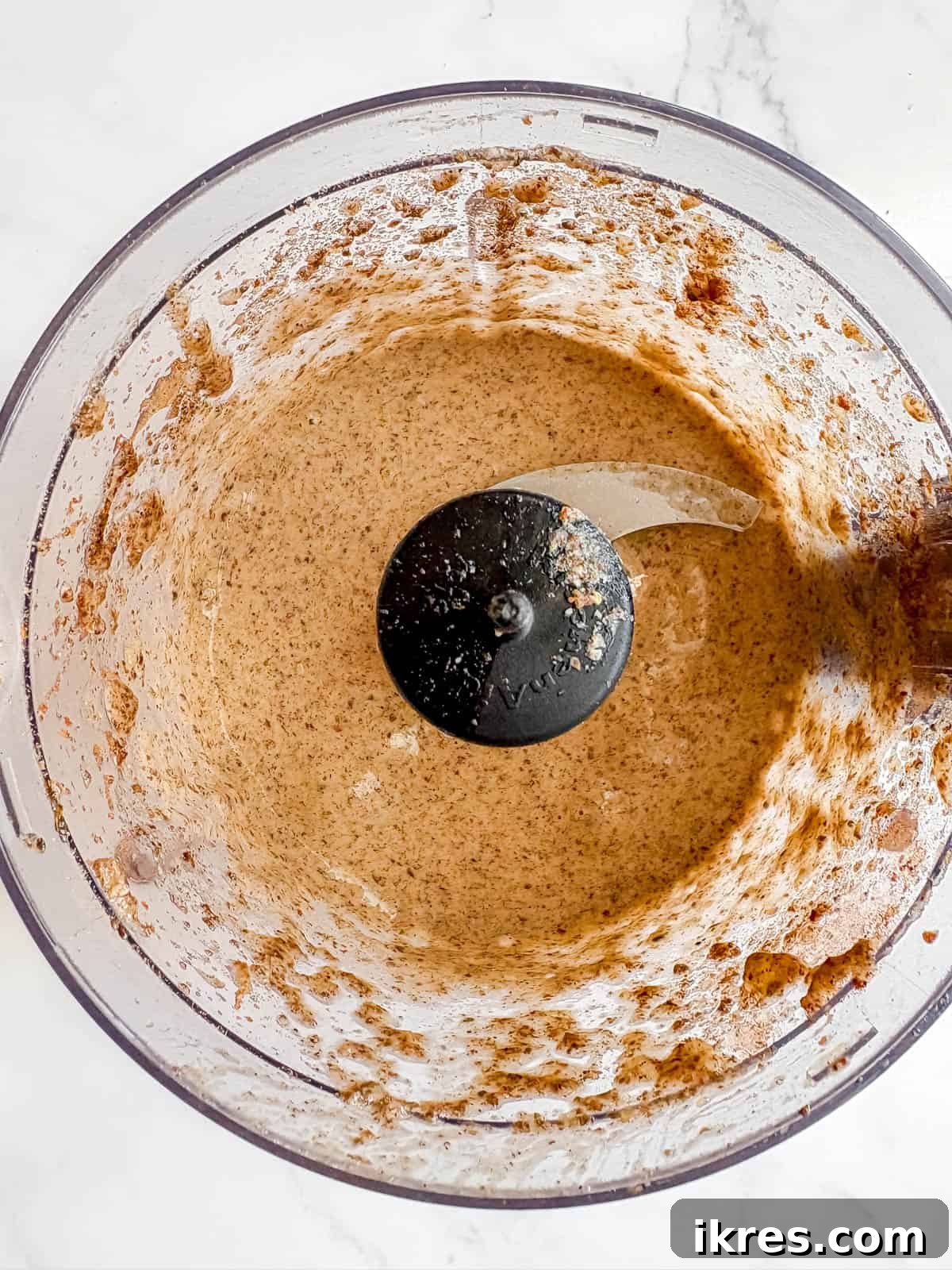 All pancake ingredients, including banana, eggs, and ground seeds, being blended together in a food processor to form a smooth batter.