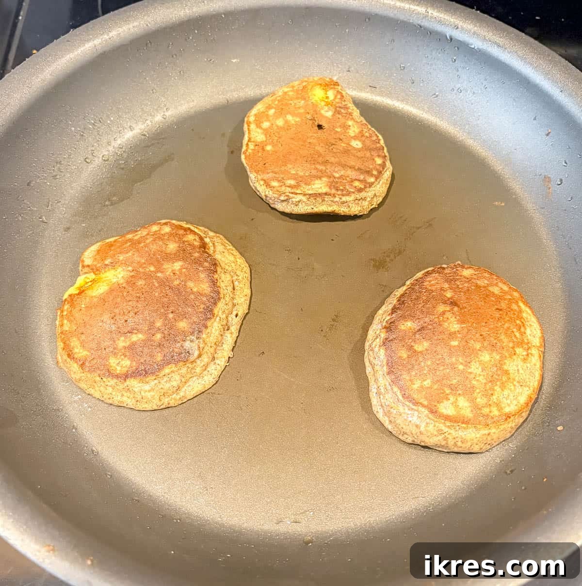 A pancake being flipped on a hot griddle, revealing a golden-brown underside, indicating it's ready to cook on the second side.