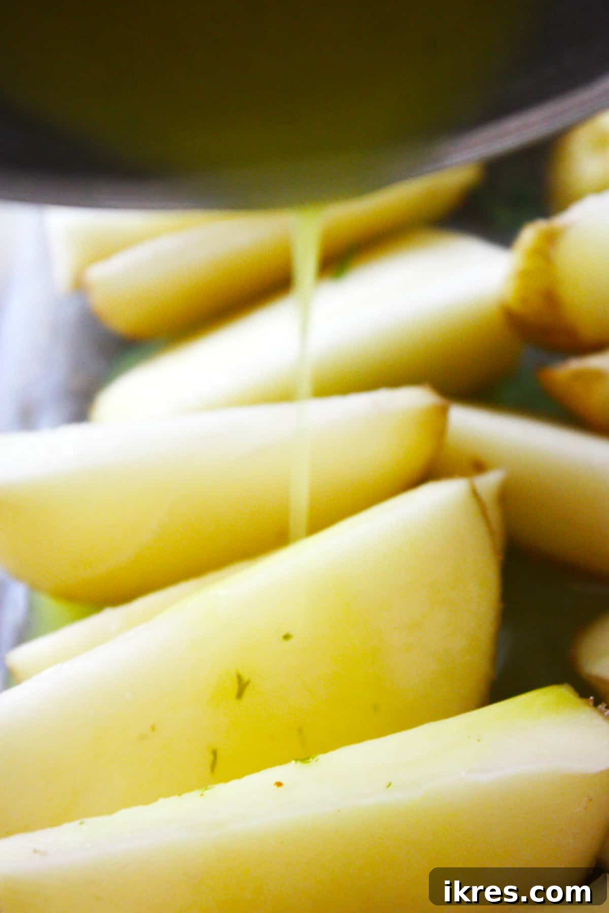 Wedges of potatoes in a pan with butter sauce being drizzled over it.