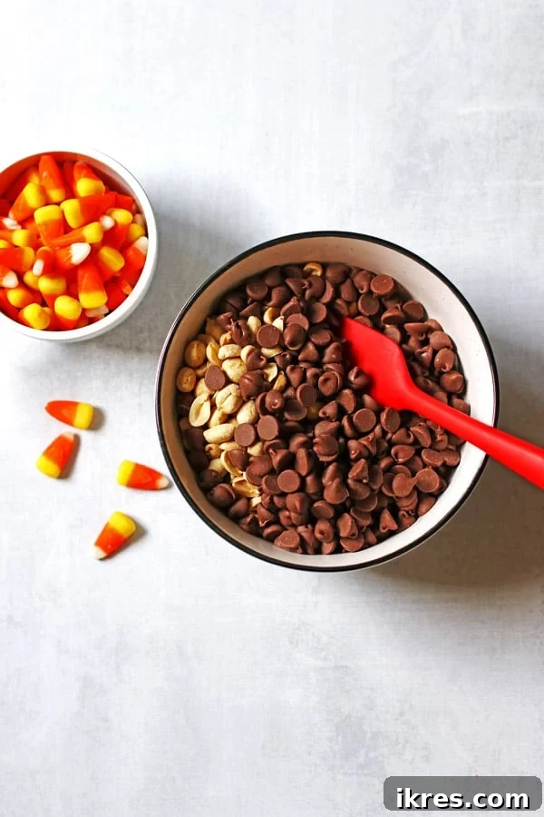 Sweet & Salalty Candy Corn Crunch 4 Chocolate chips and peanuts in a large white bowl, with candy corn being measured in a cup beside it.