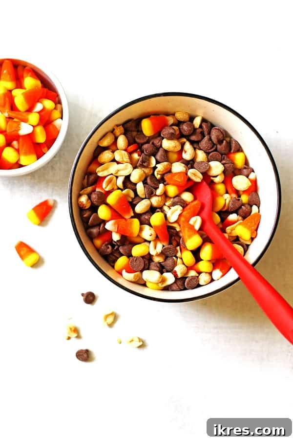 Sweet & Salalty Candy Corn Crunch 5 Mixing together the candy corn, chocolate chips, and peanuts in a bowl with a large red spoon.
