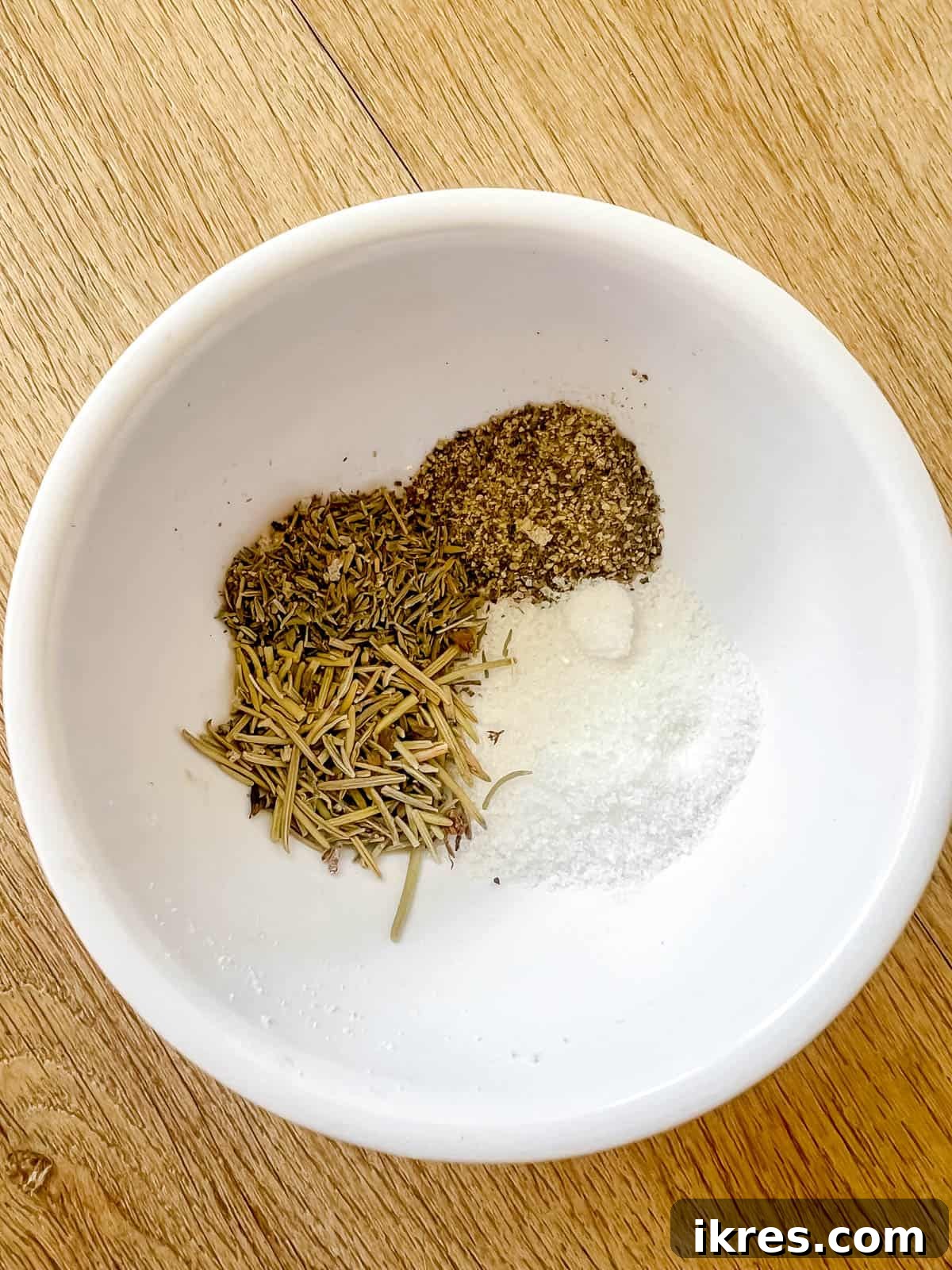 Salt, pepper, dried rosemary, and dried thyme mixed in a small white bowl.