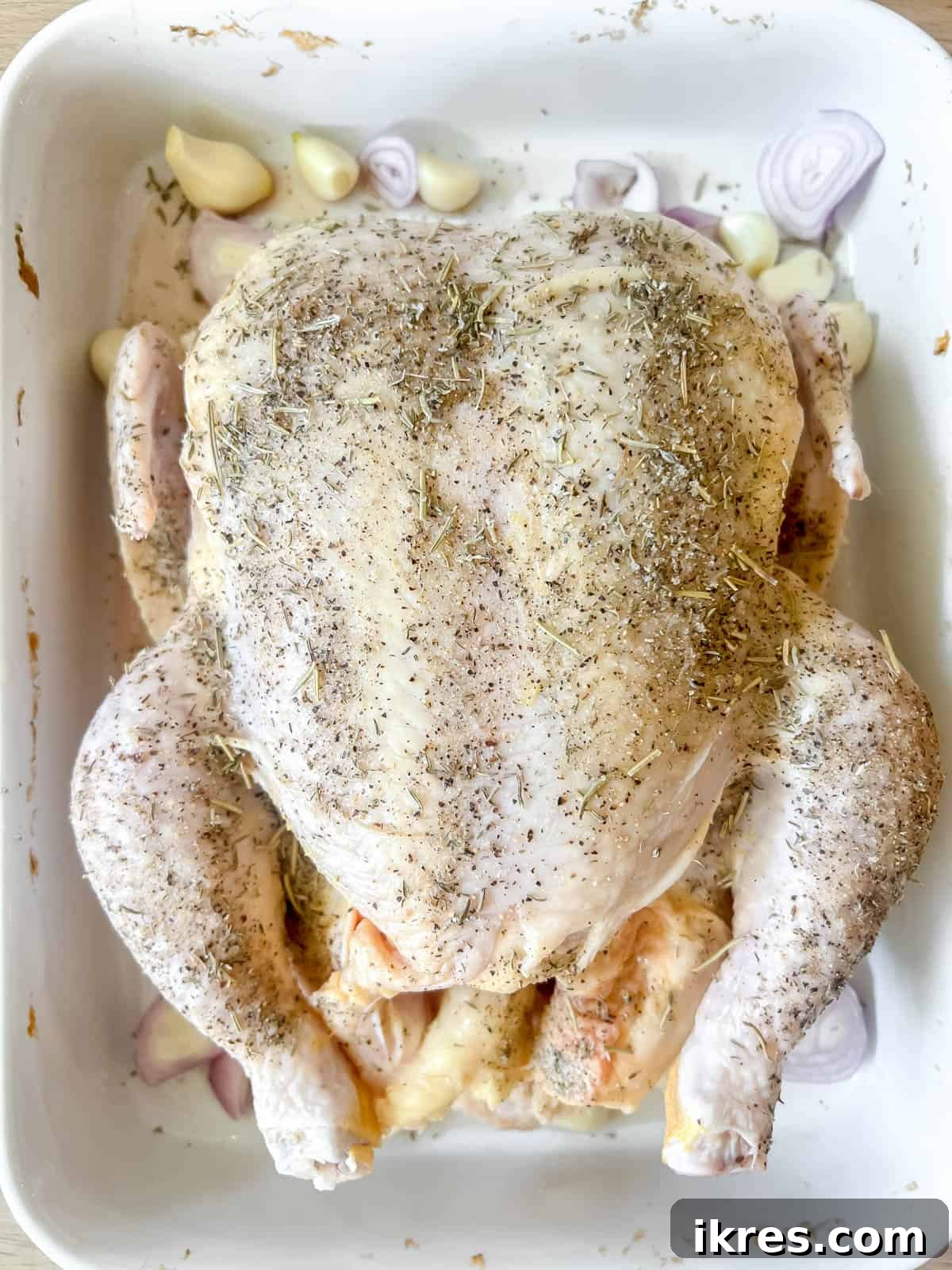 Peeled garlic cloves and sliced onion pieces arranged around the raw chicken in the roasting pan.