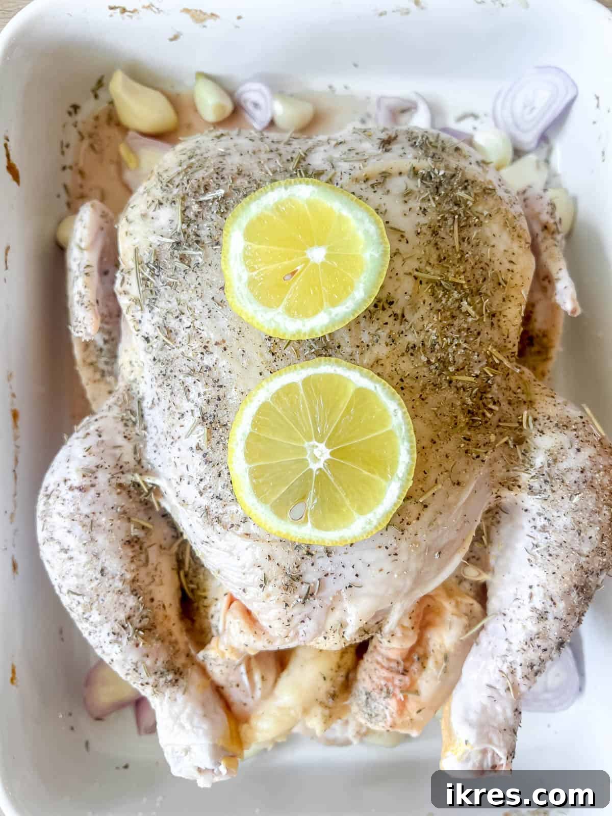 Slices of lemon placed on and around the raw chicken in the roasting pan after lemon juice has been added.