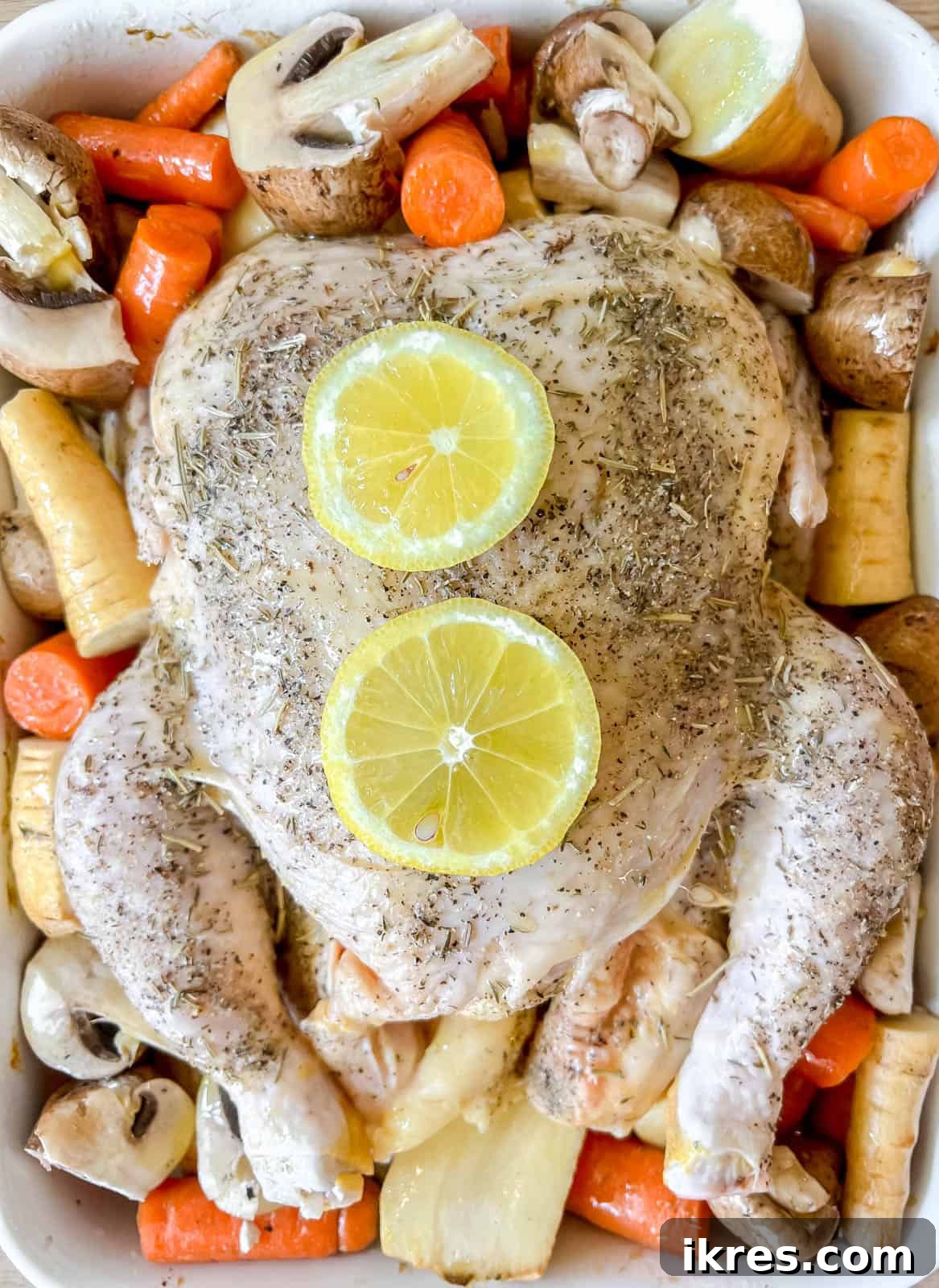 Chopped parsnips, sliced mushrooms, and large carrot pieces added to the roasting pan, surrounding the raw seasoned chicken.