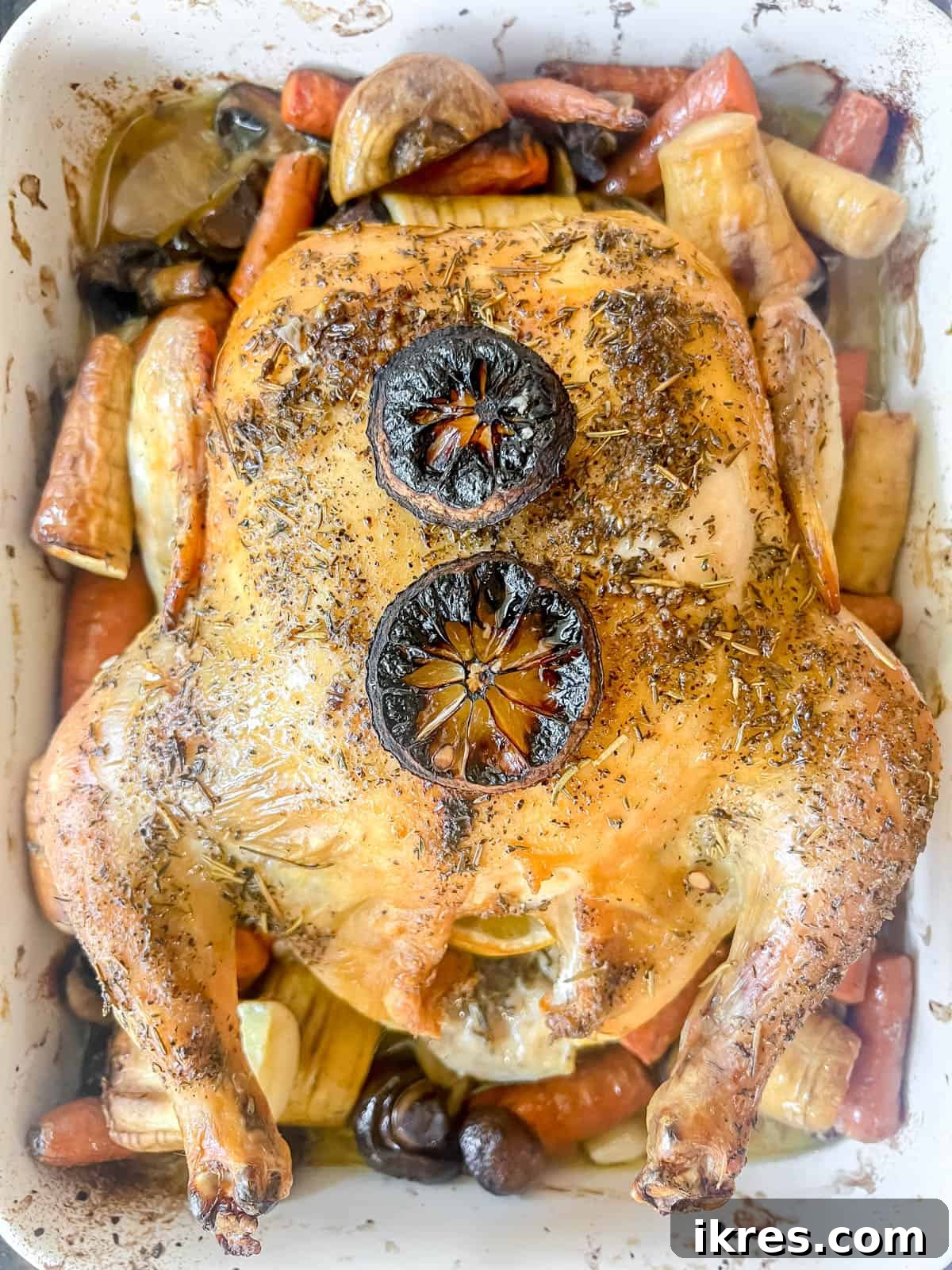 Cooked lemon thyme roast chicken, golden and juicy, surrounded by caramelized root vegetables in the roasting pan after baking.