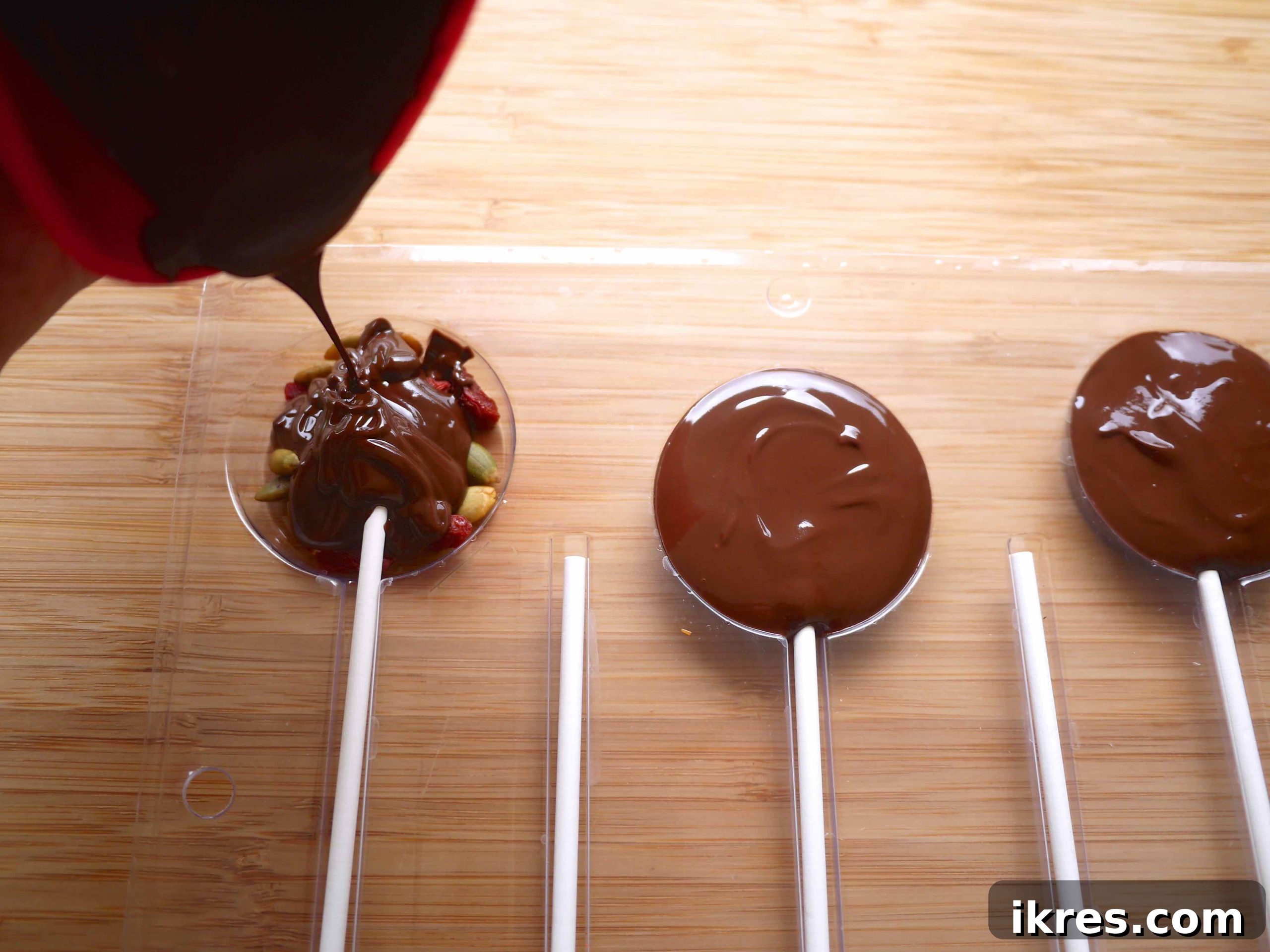Pouring melted chocolate carefully into the molds, covering the fruit, nuts, and sticks.