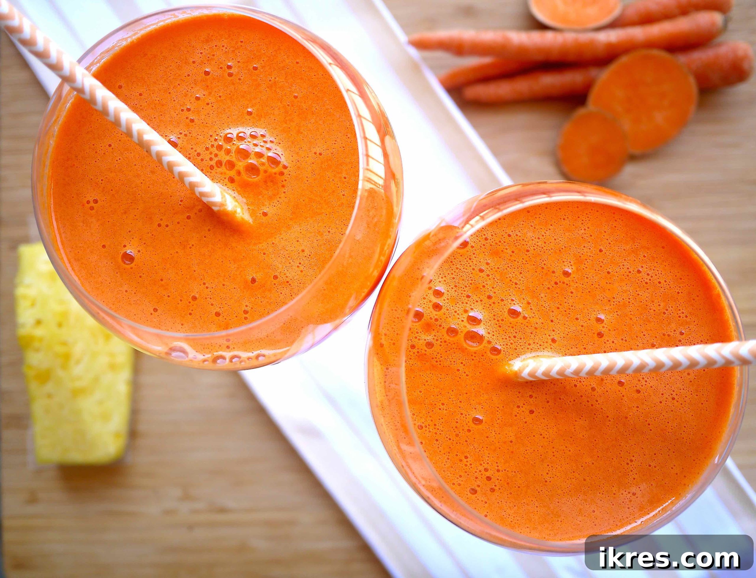 Two glasses filled with freshly made mango carrot juice, garnished with lemon slices, on a wooden surface.