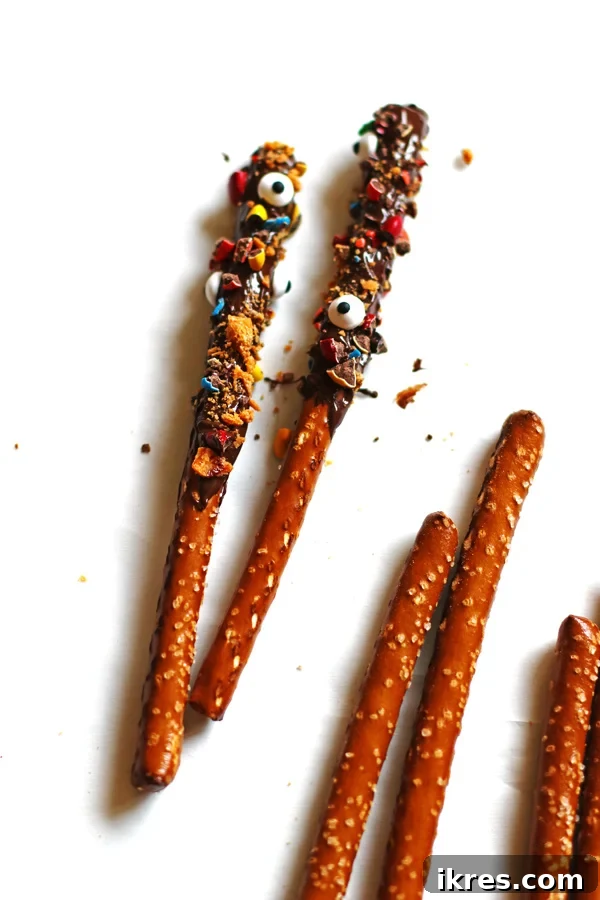 Sweet and Salty Chocolate Pretzel Rods 5 A mix of finished chocolate covered pretzel rods with various toppings next to plain pretzel rods on a white background.